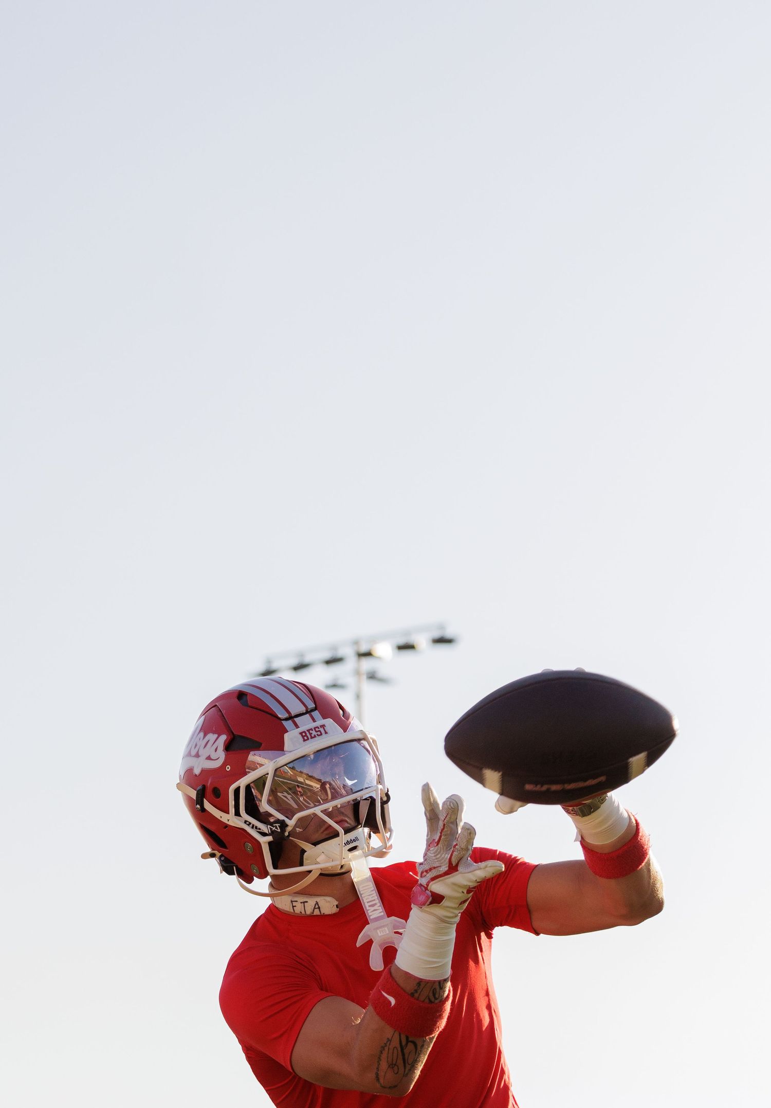 Football player in red uniform and helmet catches a pass during practice under a clear sky.