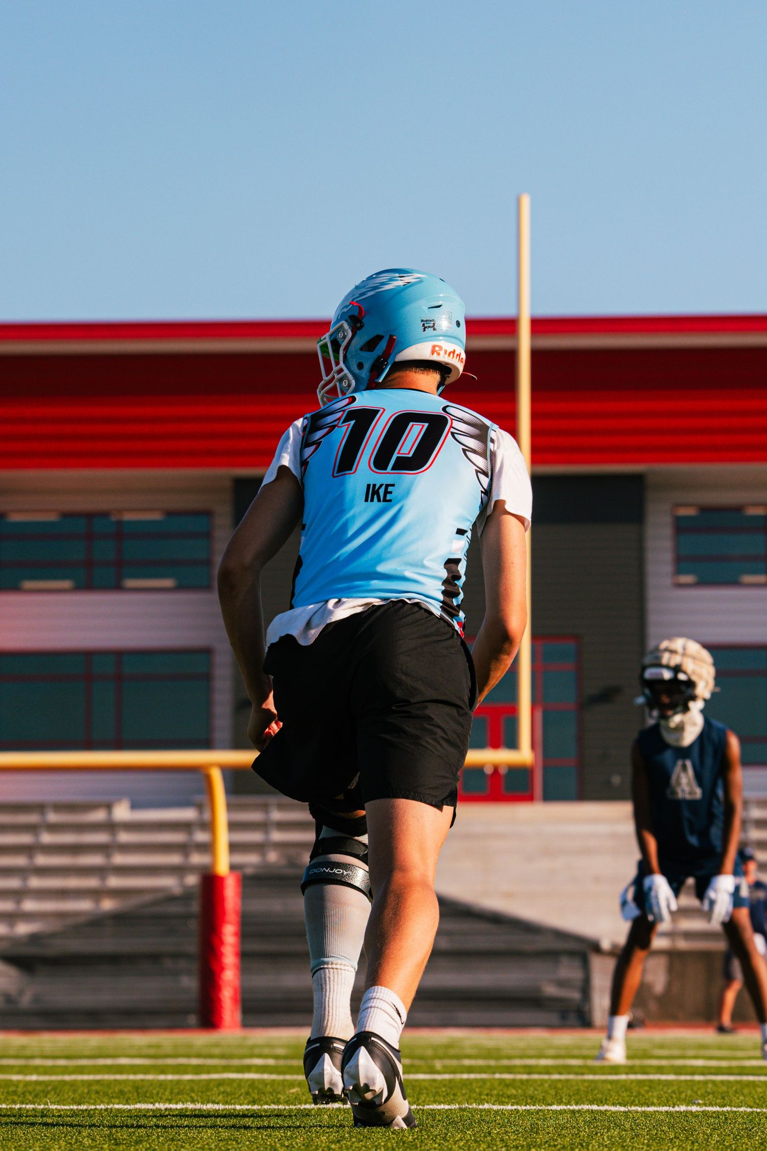 Youth football player wearing number 10 IKE jersey walks on the field during an outdoor practice session.