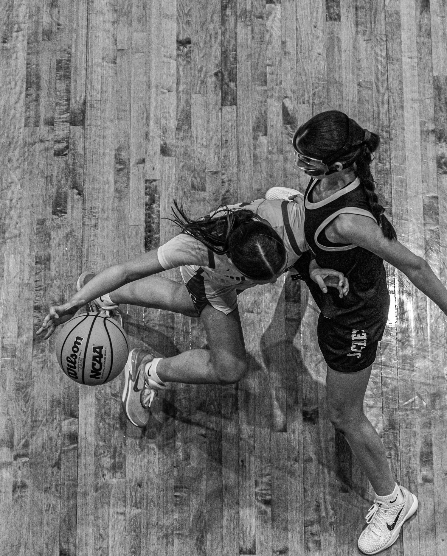 Aerial black and white photo of two female basketball players competing for the ball.