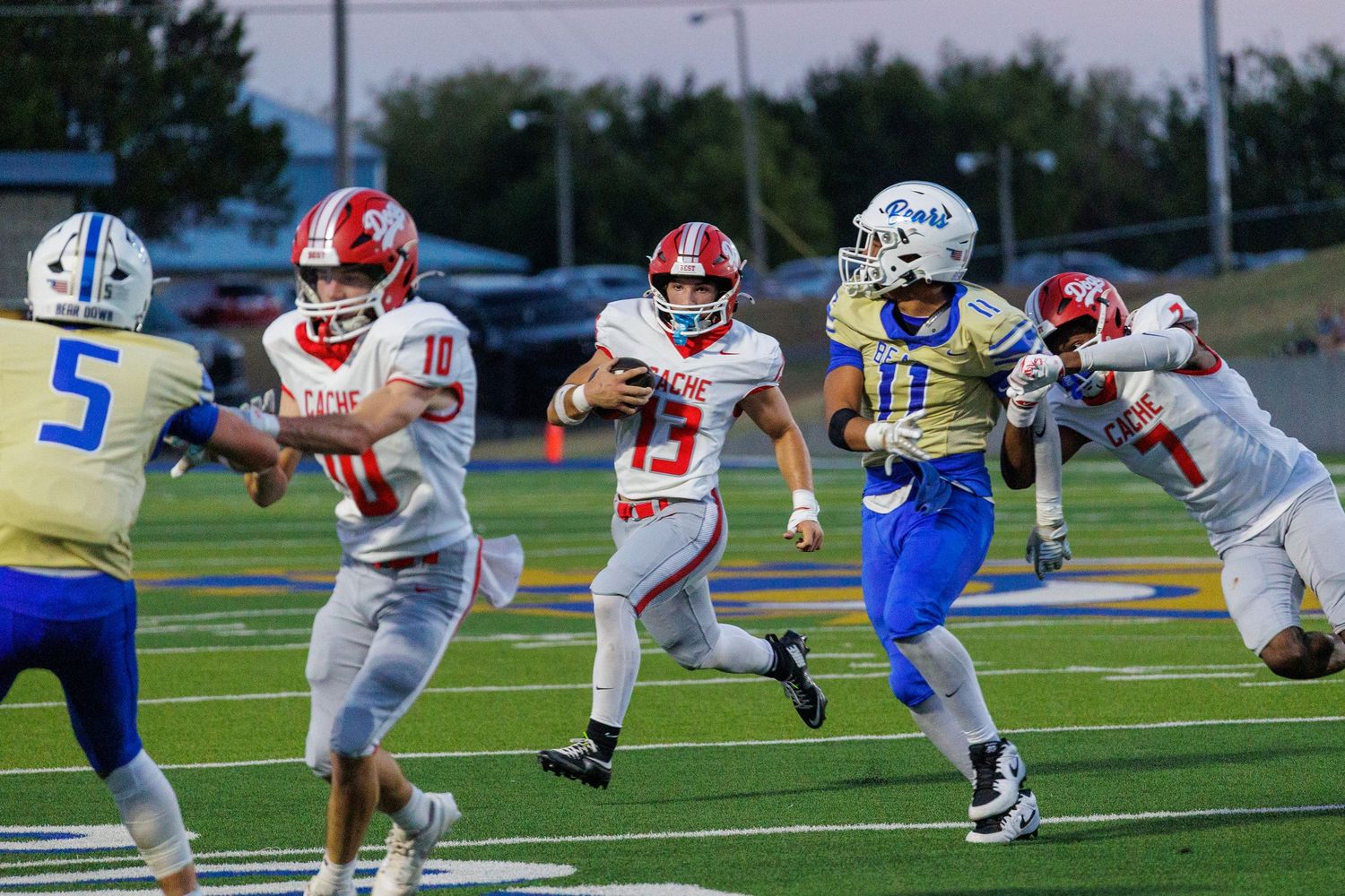 High school football players in red and white uniforms run plays against opponents in blue and gold during a night game.