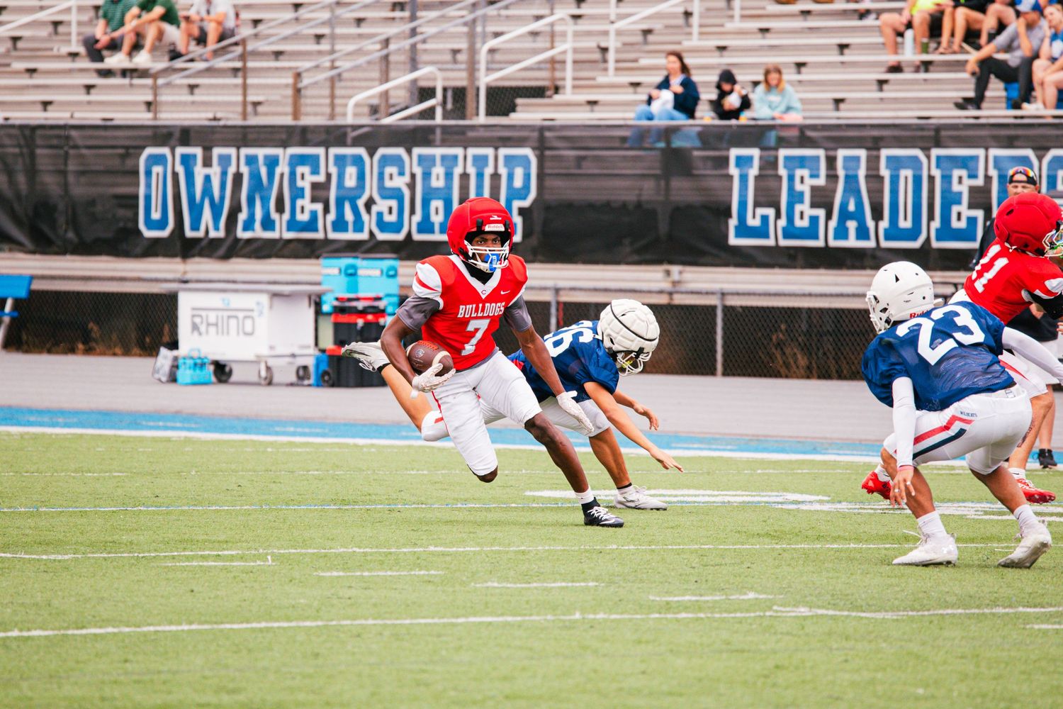 A Bulldogs football player in red uniform runs with the ball during a high school game.