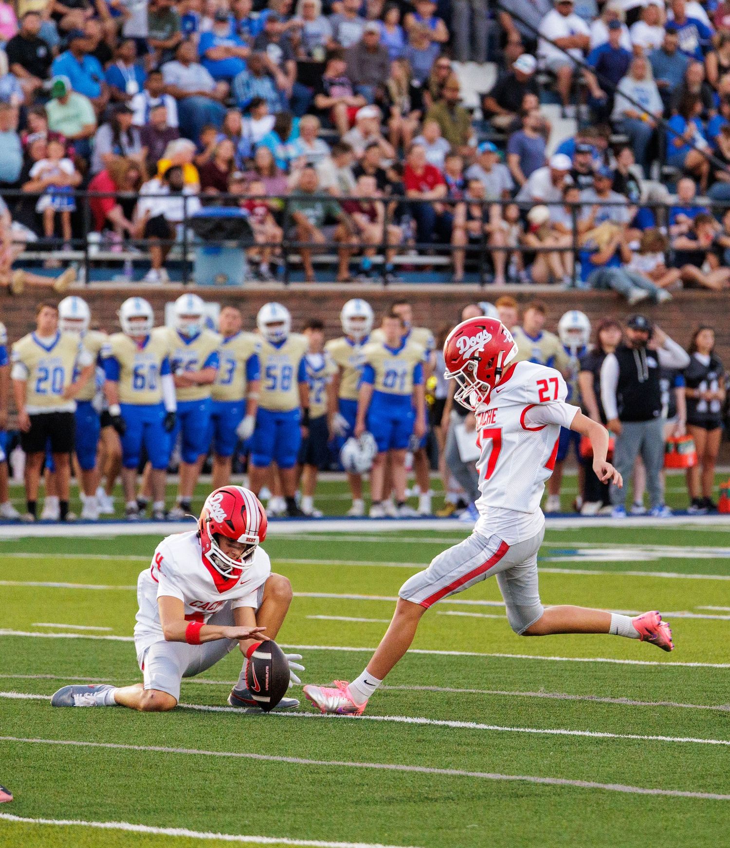 Two football players in red uniforms execute a field goal kick during a high school game.