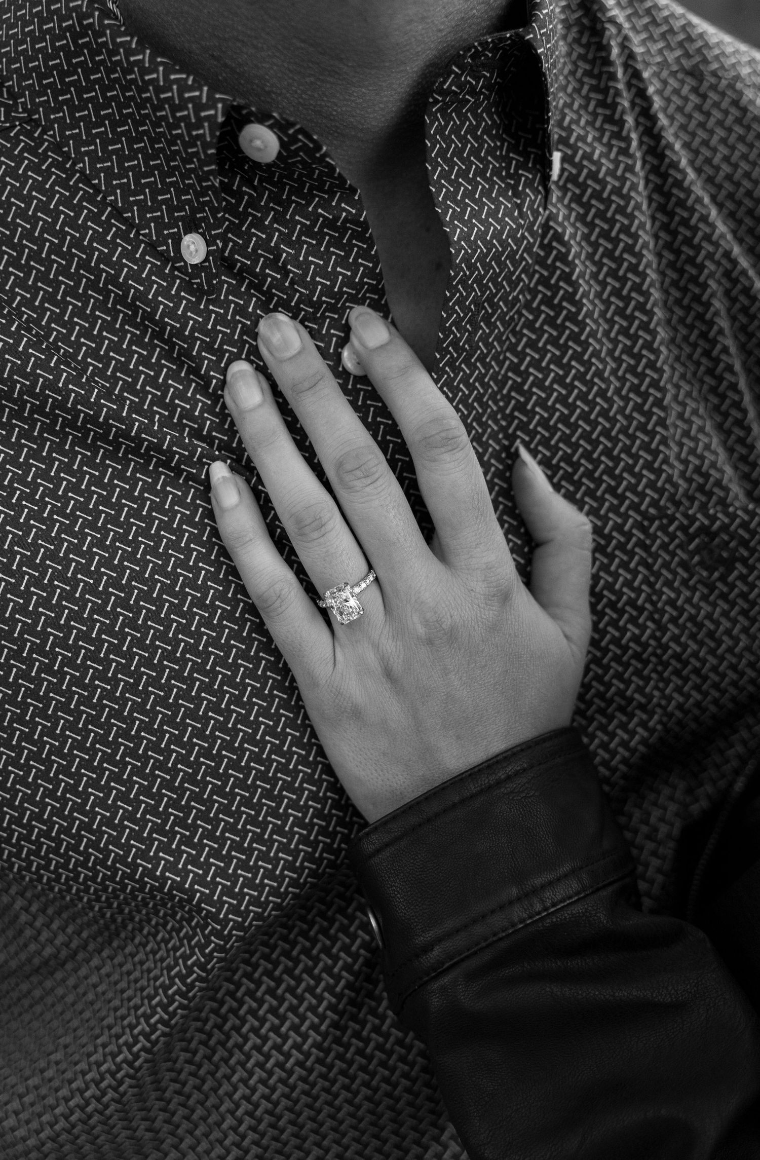 Black and white close-up of a womans hand displaying an engagement ring resting on a mans chest.