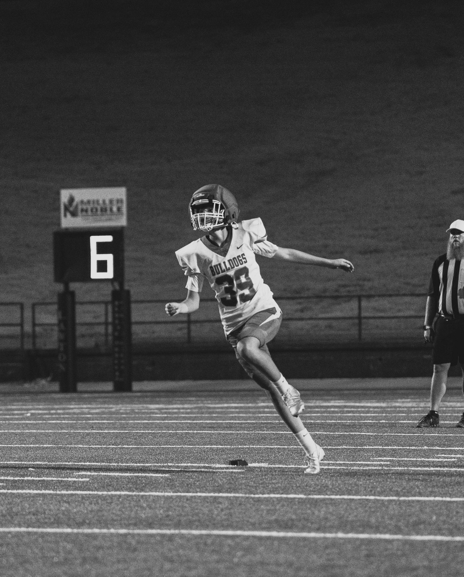 Black and white photo of a football player wearing jersey number 39 running on a field during a night game.