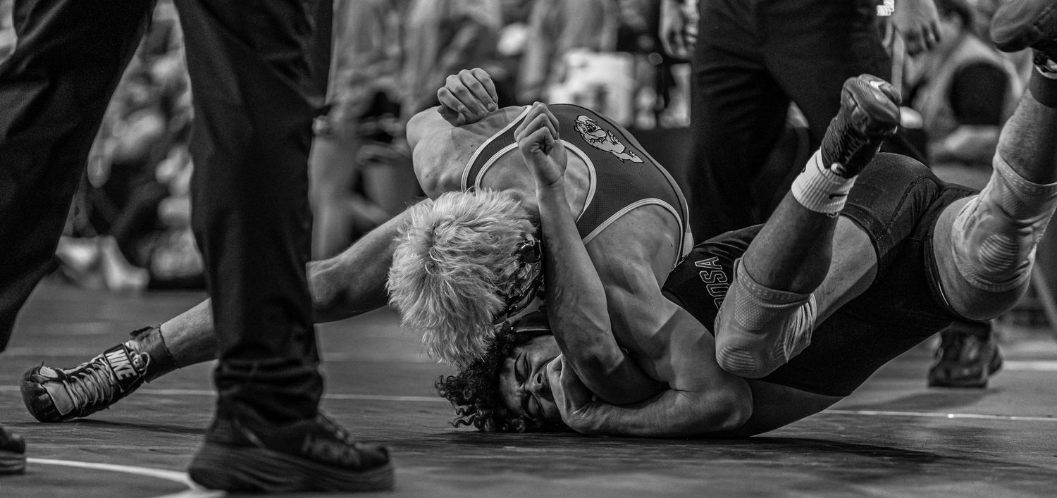 Two wrestlers grapple on the mat in a black and white action wrestling match photo.