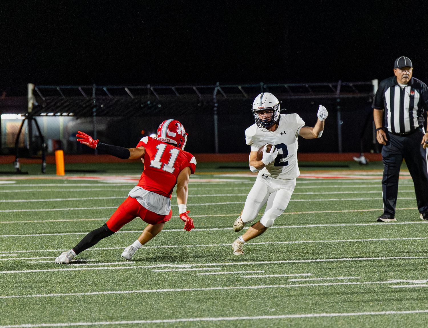 A football player in white uniform evades a defender in red number 11 jersey during a night game.