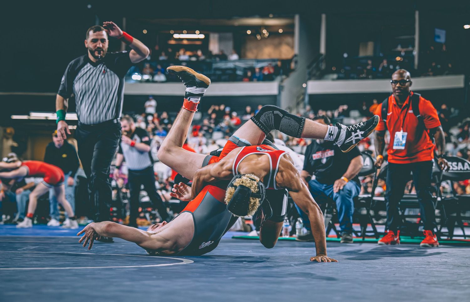 Wrestler executes a dramatic takedown throw during a competitive wrestling tournament in an arena.
