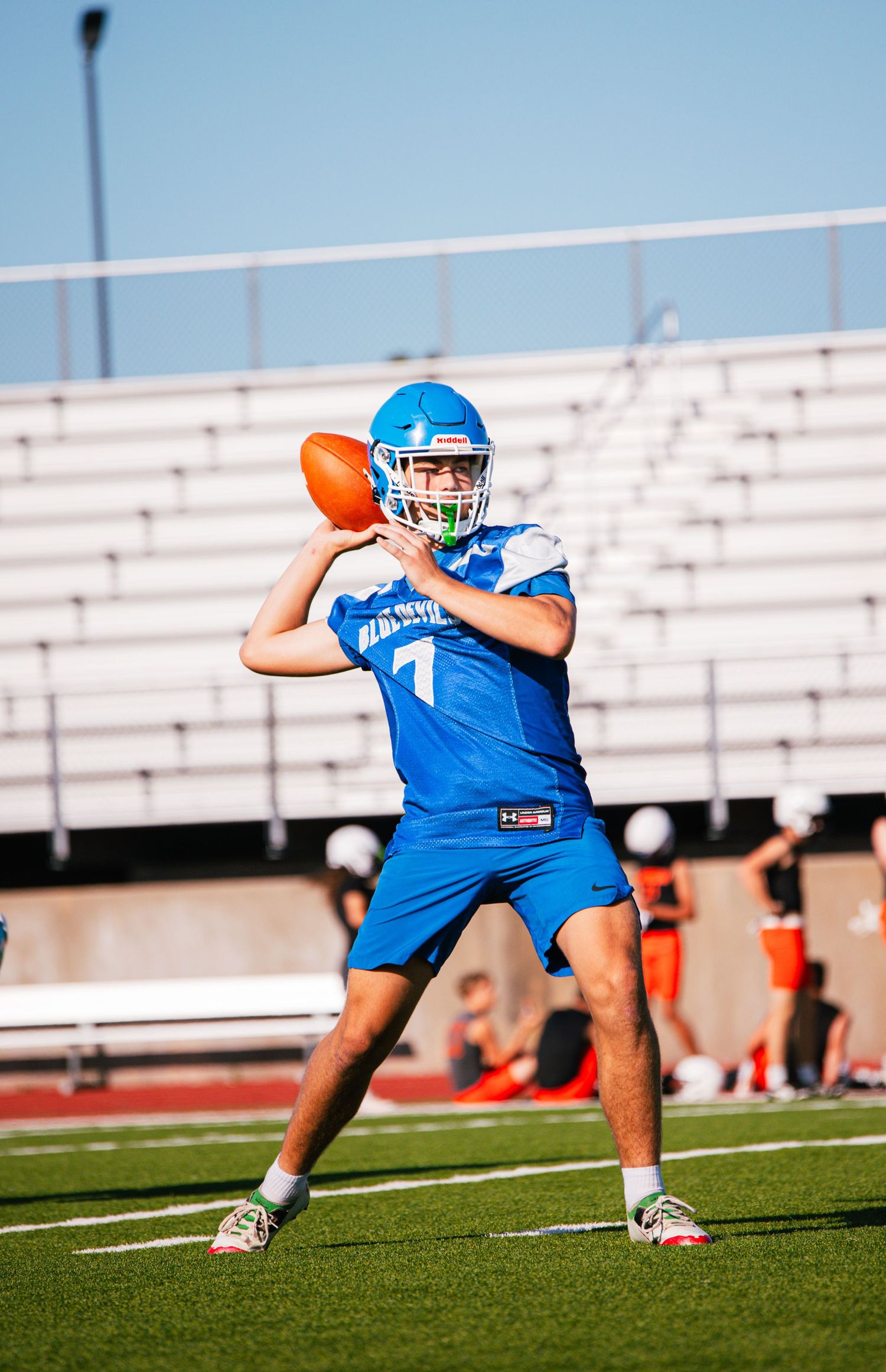 High school quarterback in blue uniform and helmet prepares to throw a football during outdoor practice.
