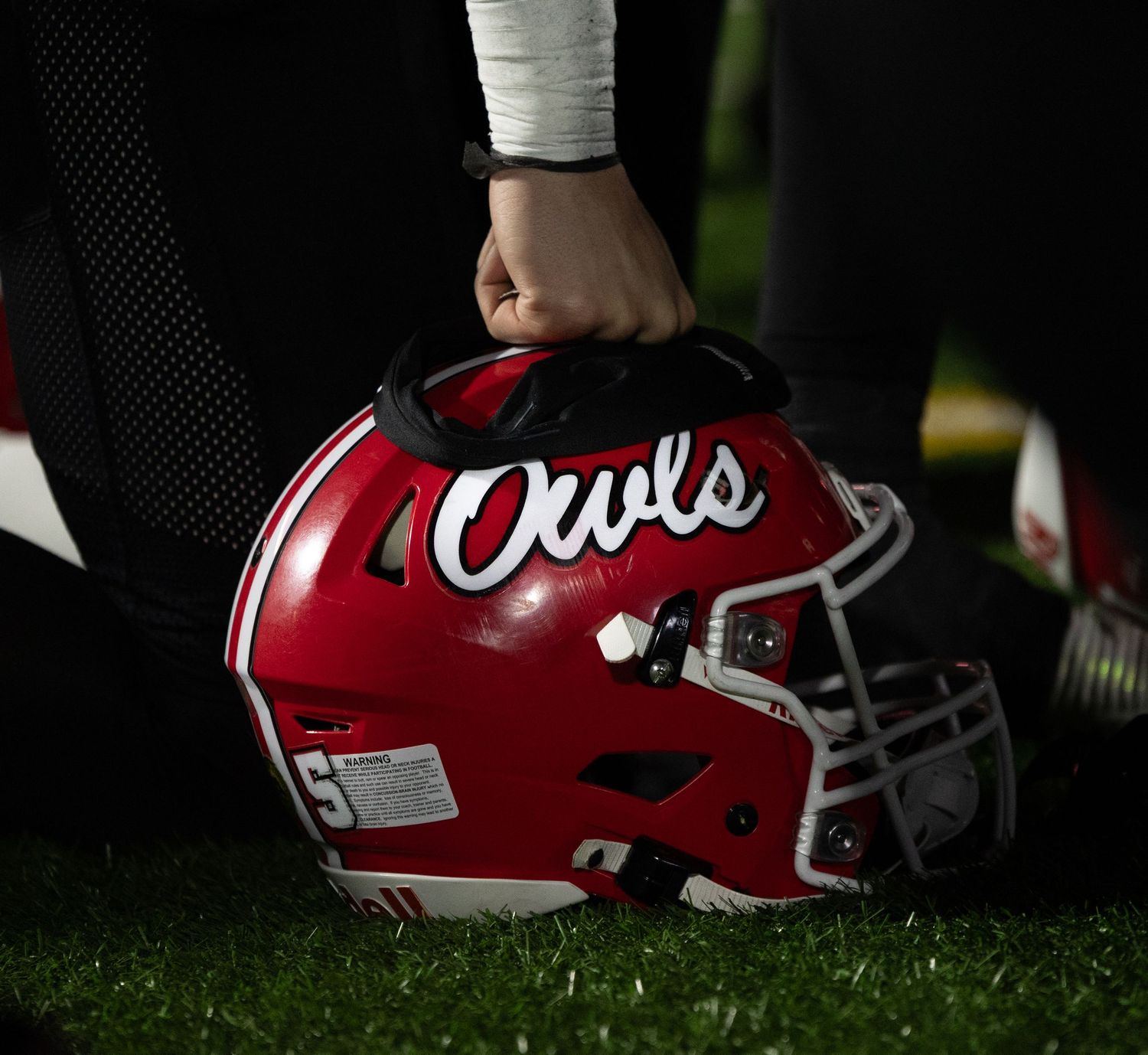 A player holds a red Owls football helmet on the sideline before a game.