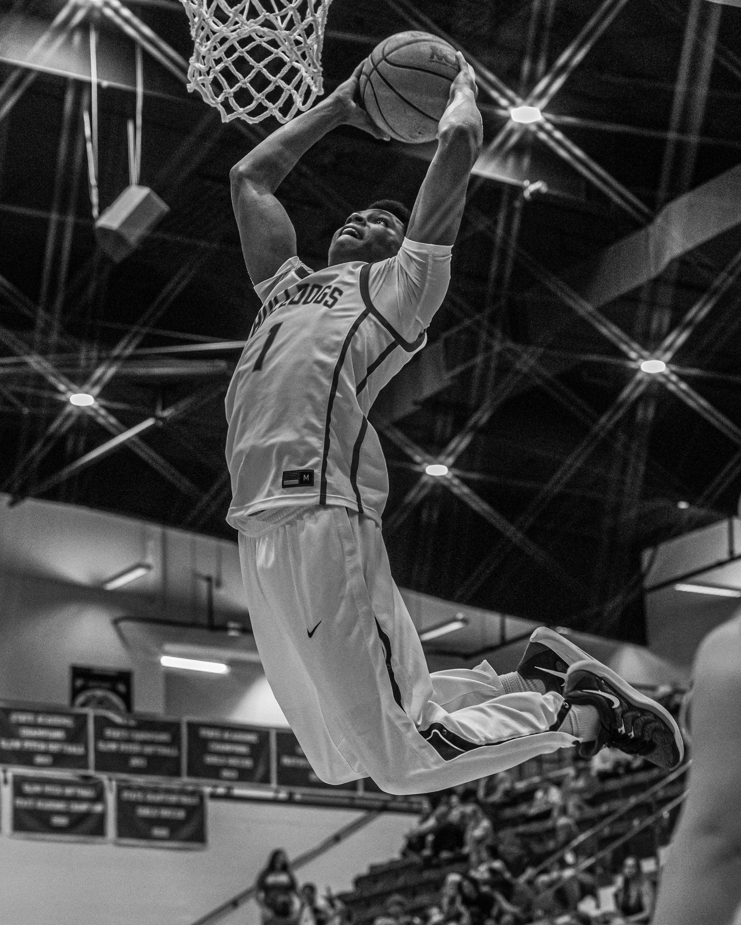 Athletic player executes powerful slam dunk in dramatic black and white indoor basketball photo.