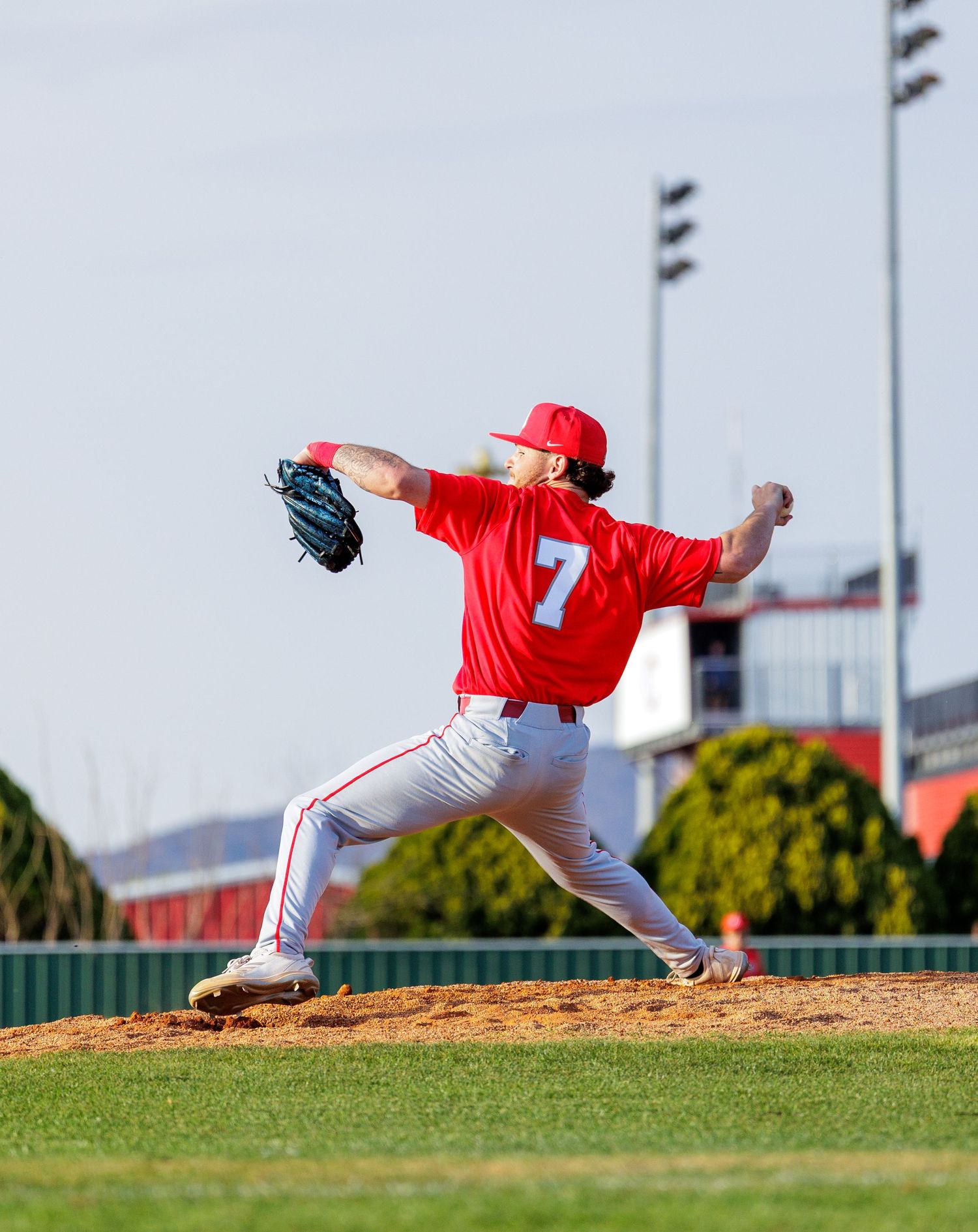 Baseball player number 7 in red uniform delivers a pitch from the mound during a game.