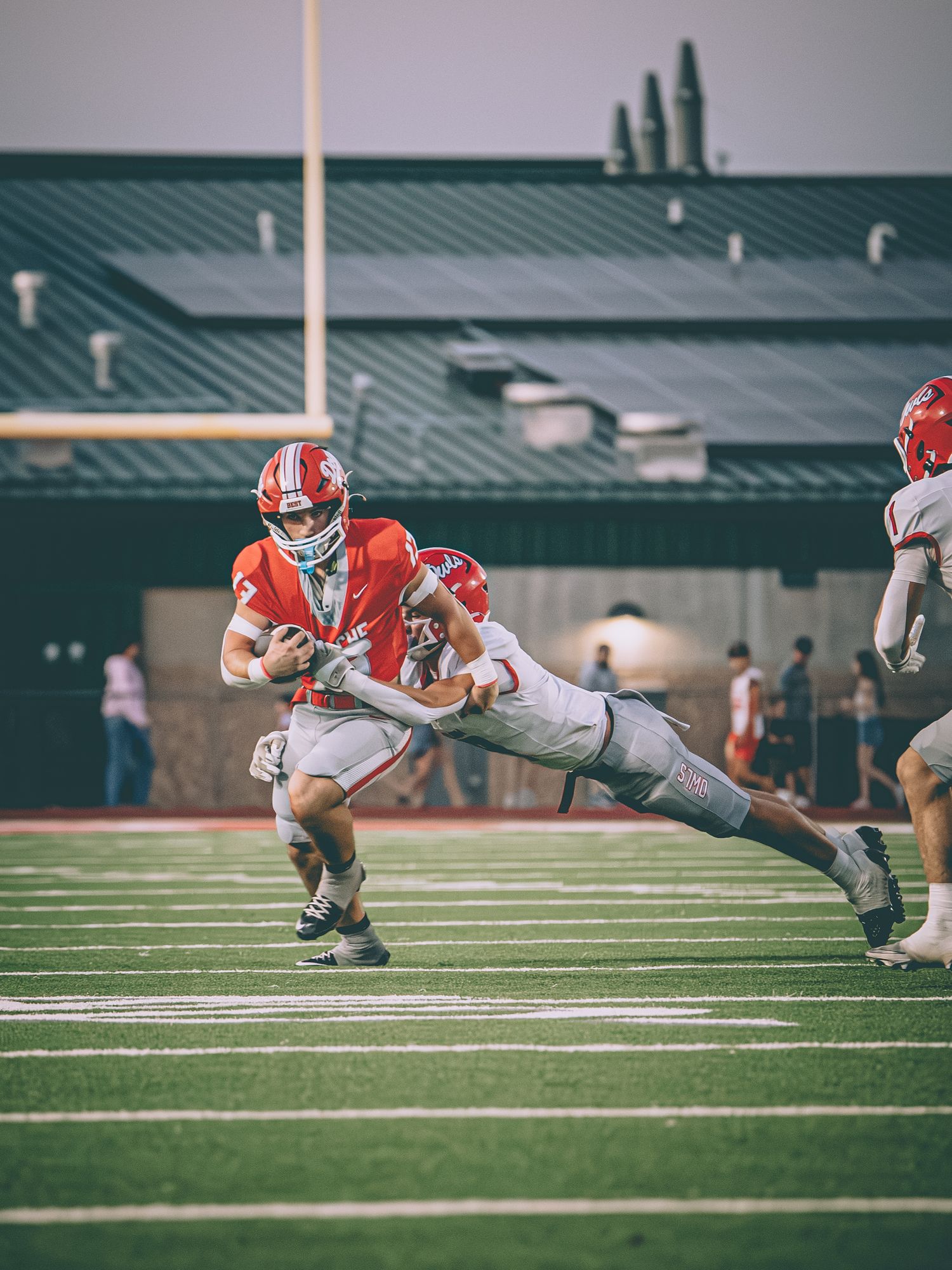 A football player in a red uniform carries the ball while being tackled by a defender during a high school game.