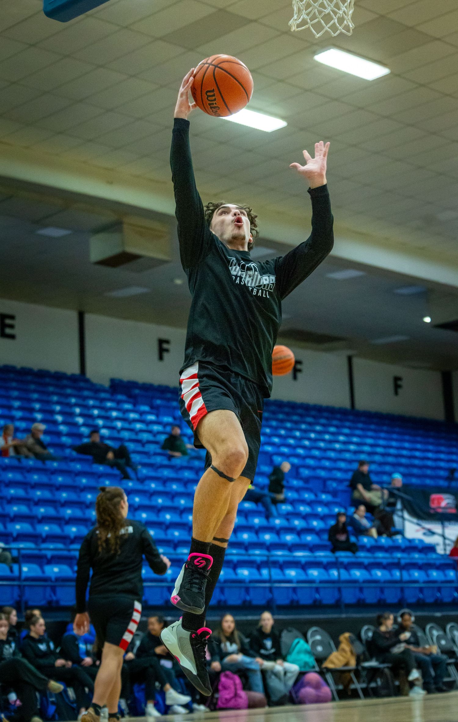 Basketball player in black uniform leaping toward the hoop for a layup in an indoor gymnasium.