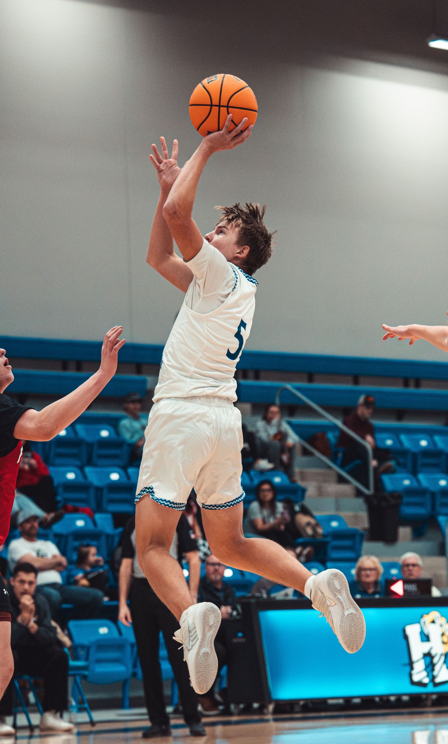 Basketball player number 5 in white uniform goes up for a layup during an indoor game.