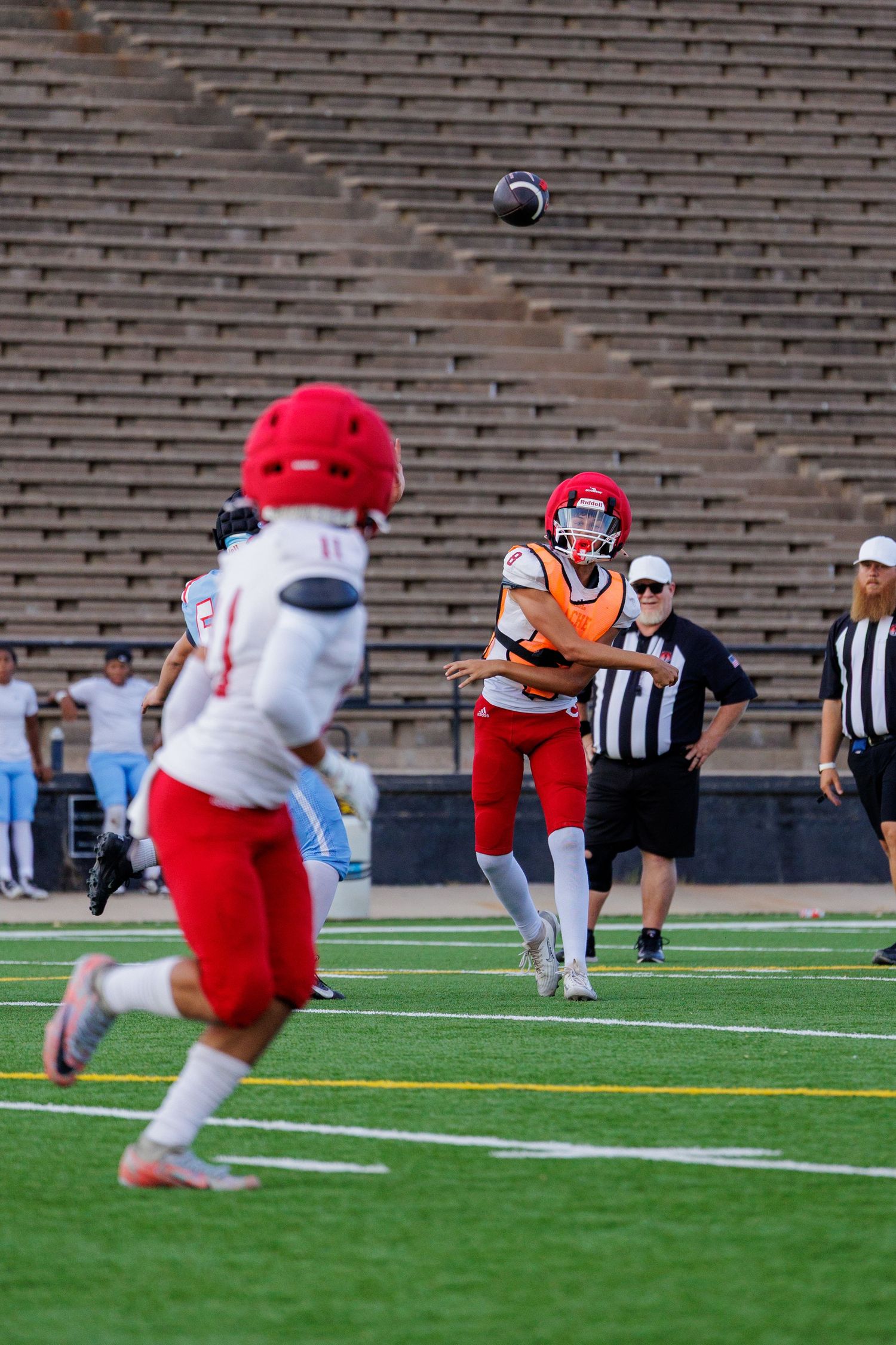 Football player in red jersey catches a pass during a game in an empty stadium with a referee nearby.