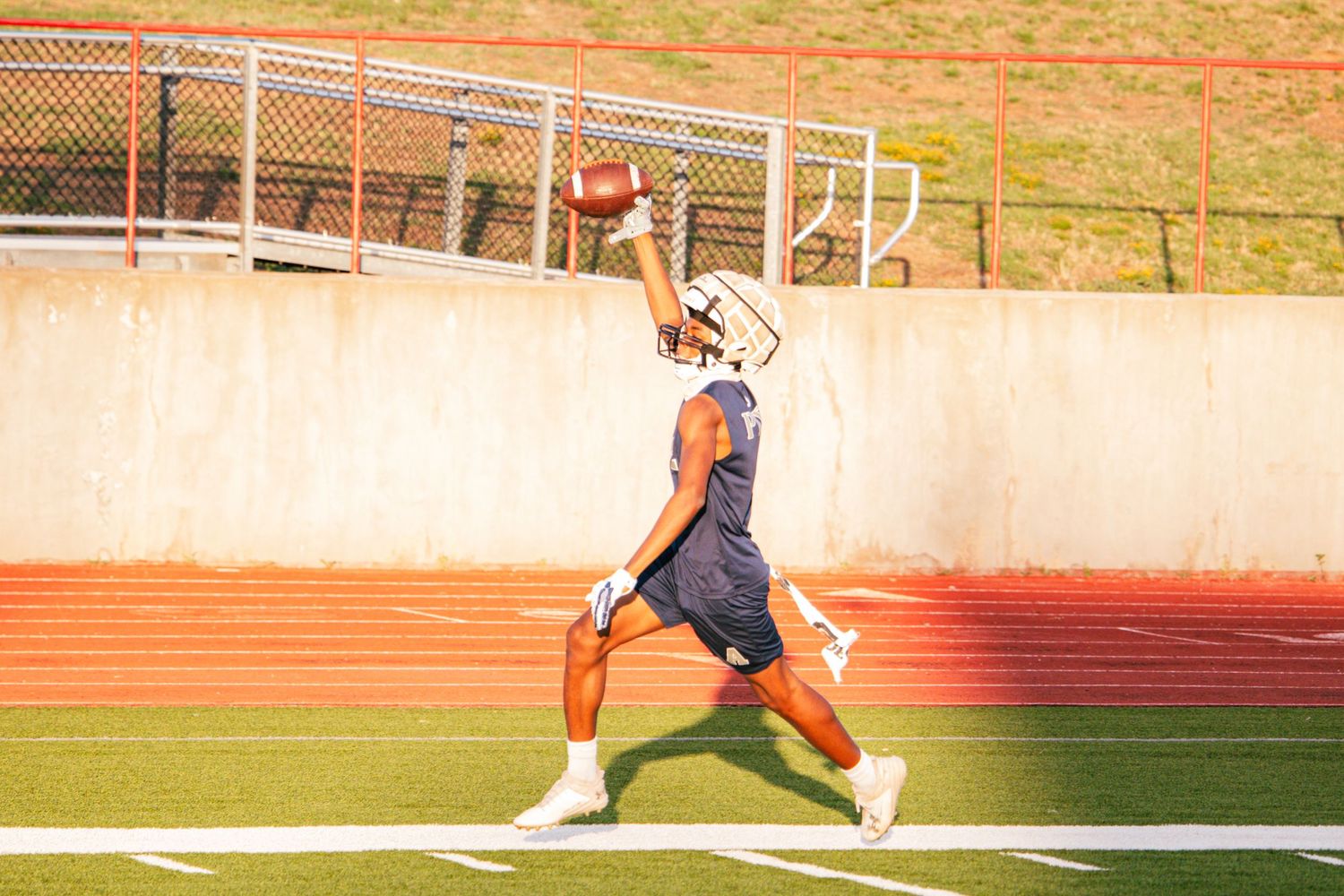 Football player in blue and white uniform stretches to make a one-handed catch on track.