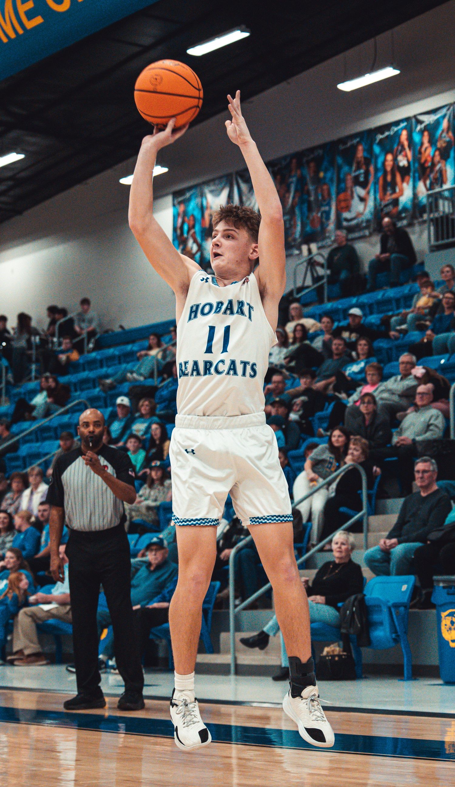 Hobart Bearcats player number 11 jumps to shoot a basketball during a home game with fans in stands.