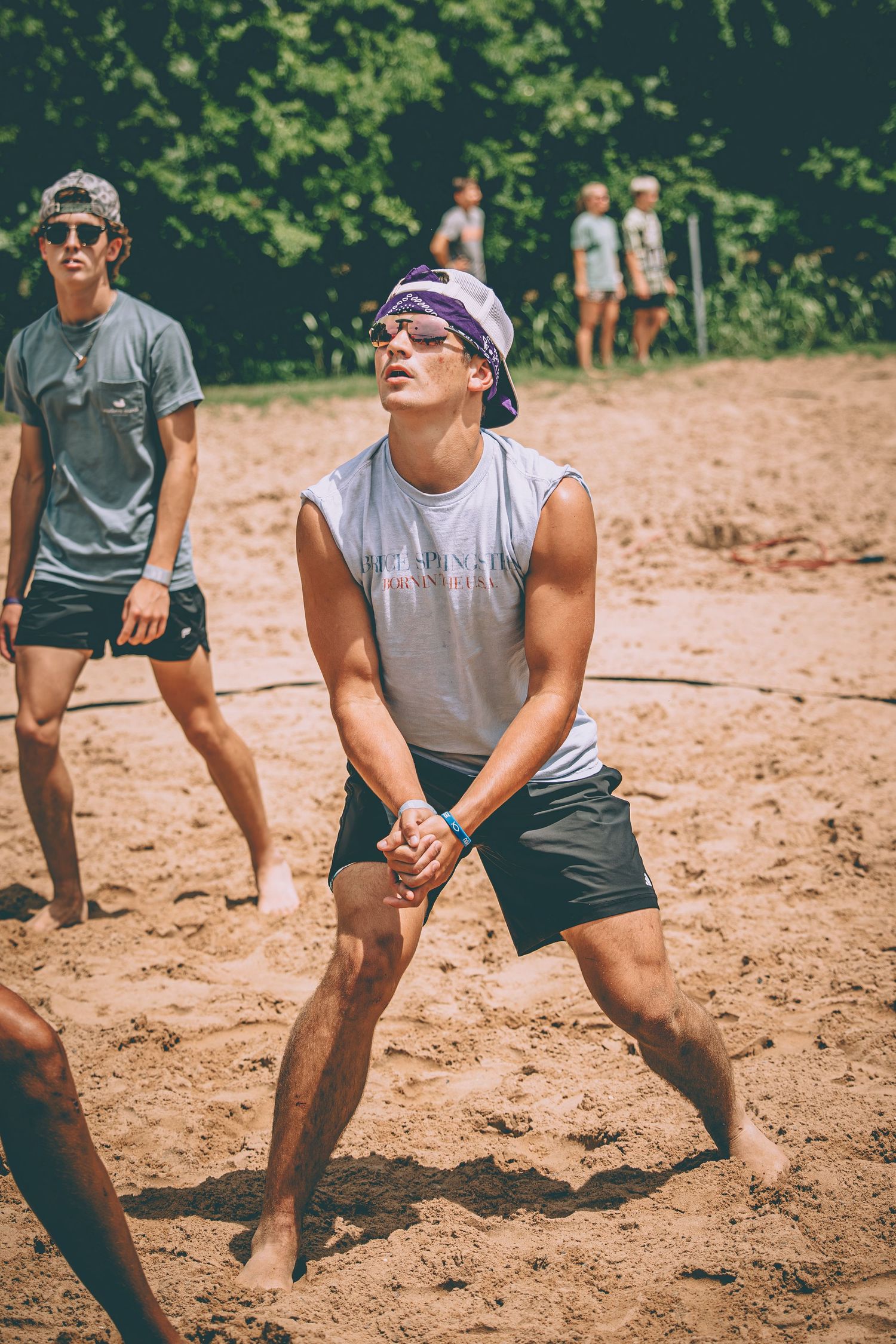 Young man in a bandana playing beach volleyball on a sandy court in summer.
