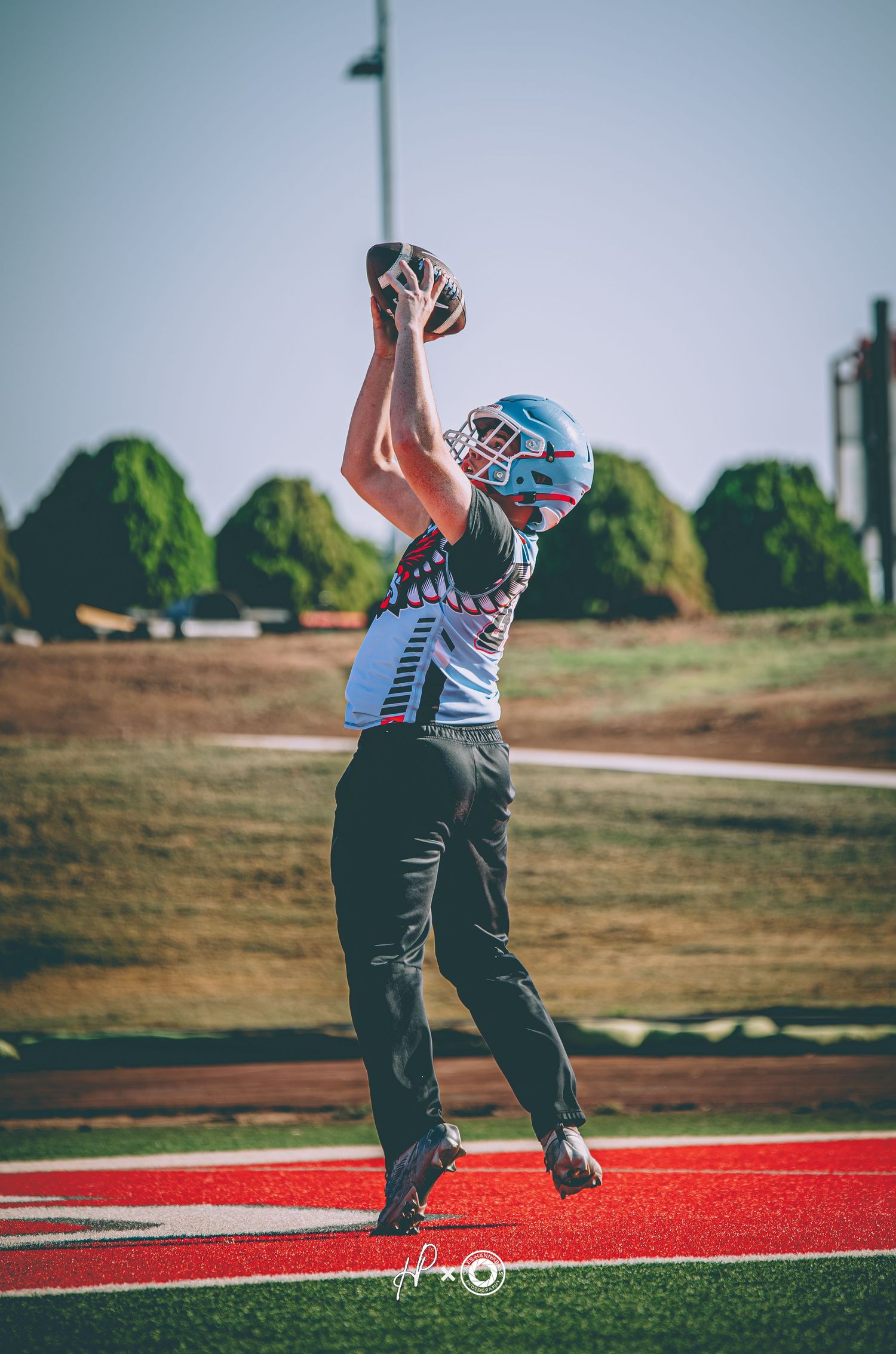 Football player catches ball in end zone wearing blue helmet and red uniform on a sunny day.