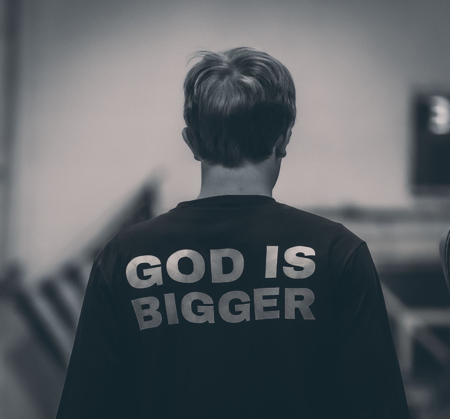 Person wearing black sweatshirt with 'God Is Bigger' text on back, black and white photography.