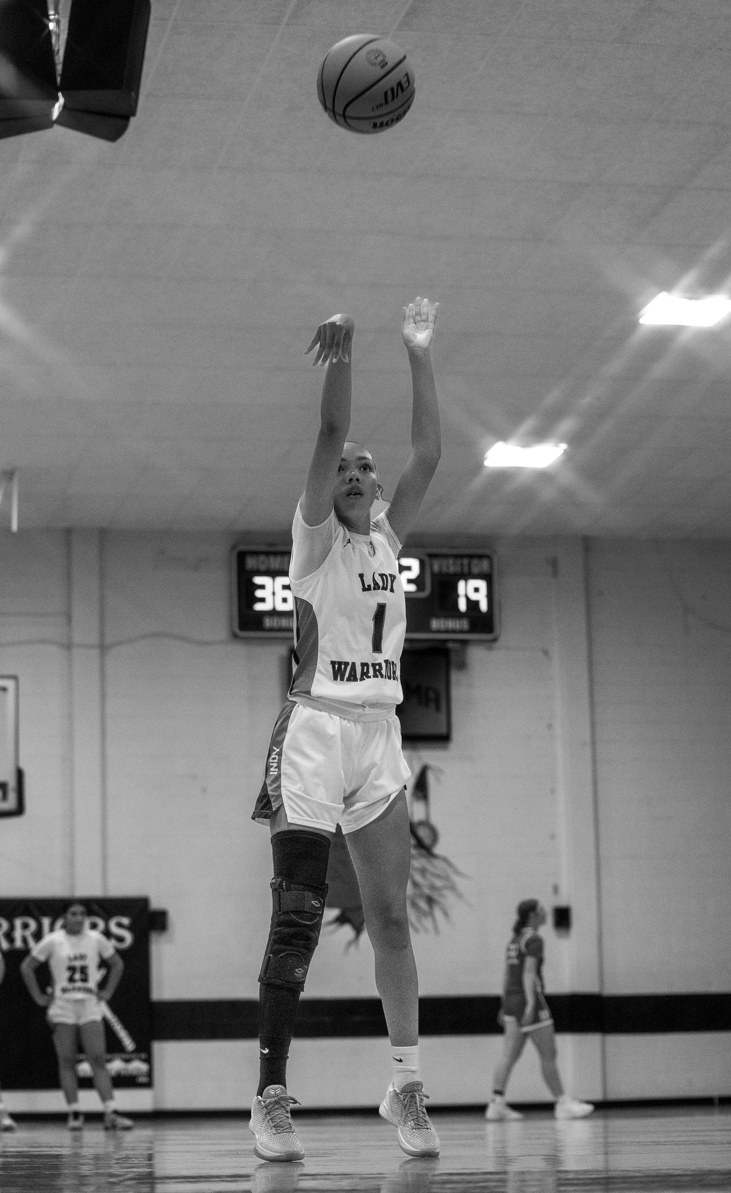Female basketball player wearing number 1 Lady Warriors jersey shoots a jump shot during an indoor high school game.