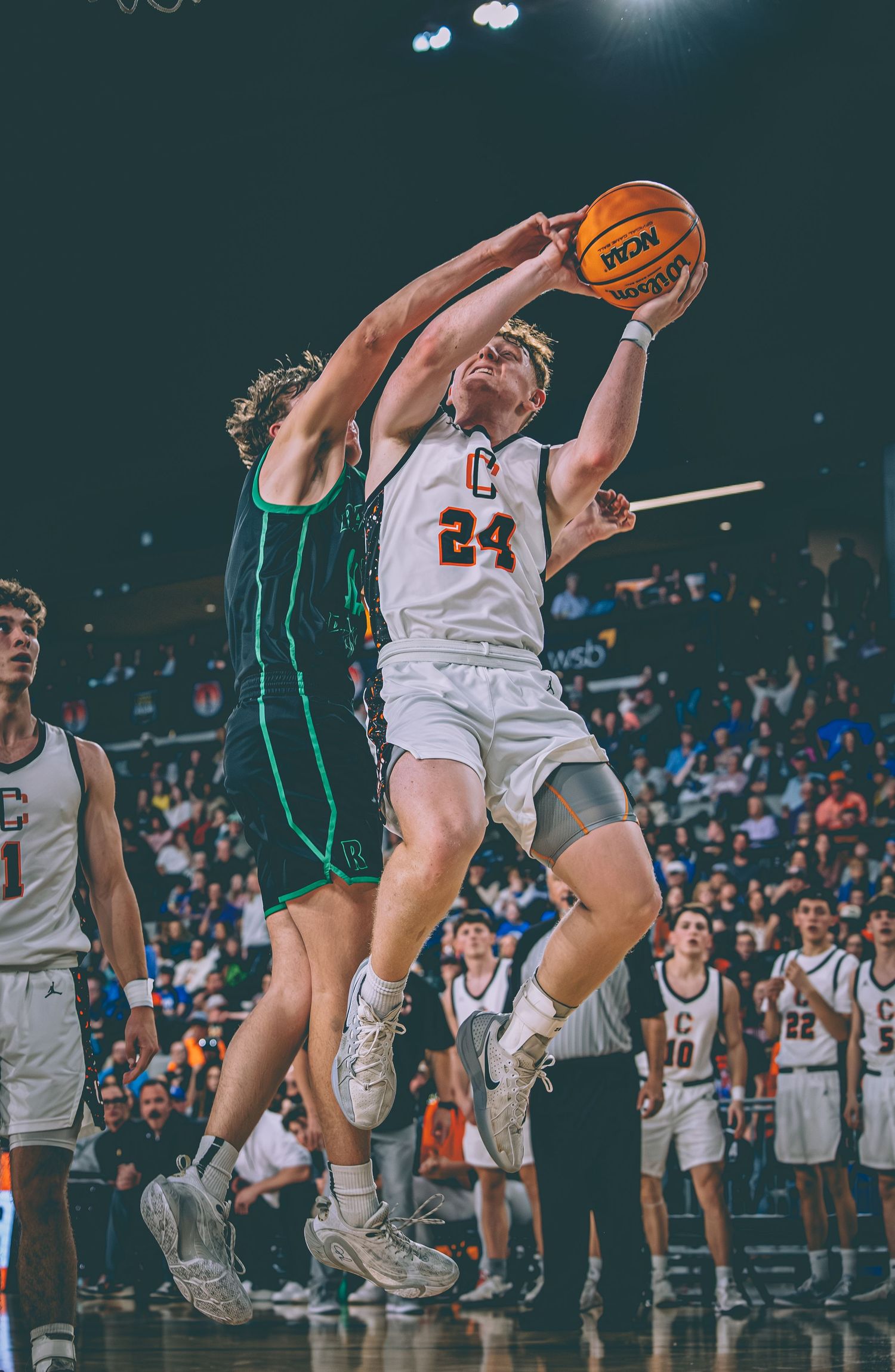 Basketball player #24 attempts a layup while being fouled by a defender in a crowded arena.