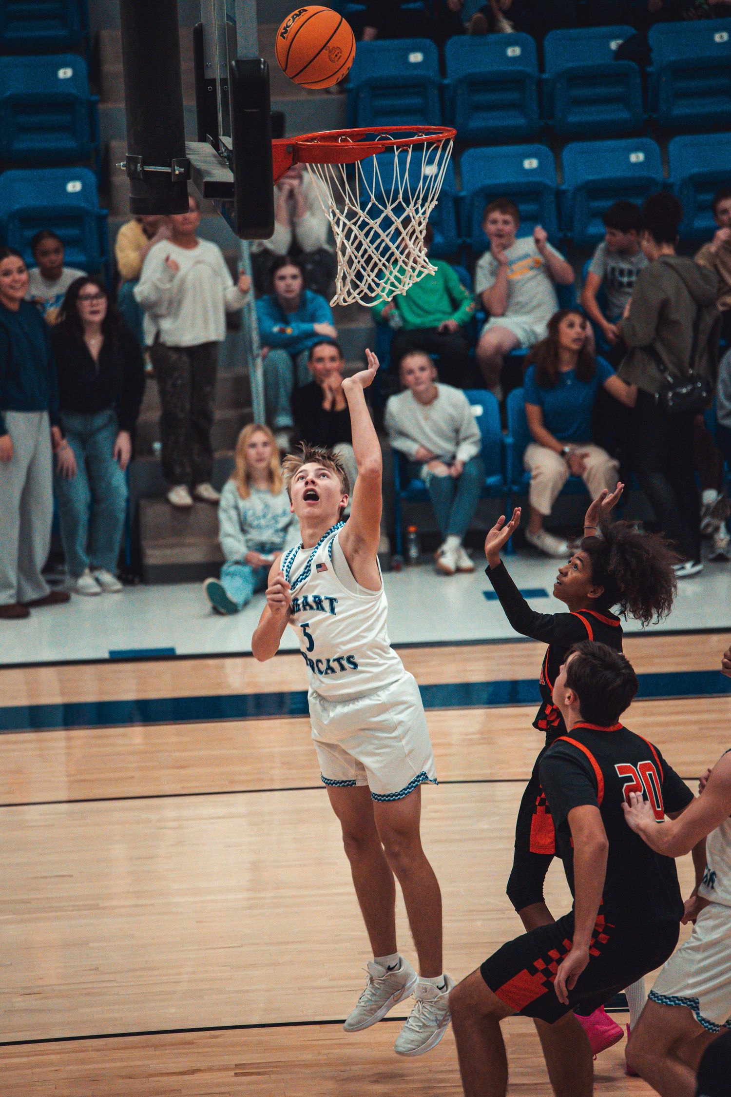 Hobart Bearcats player drives to the basket for a layup against red-uniformed defenders in a packed gym.