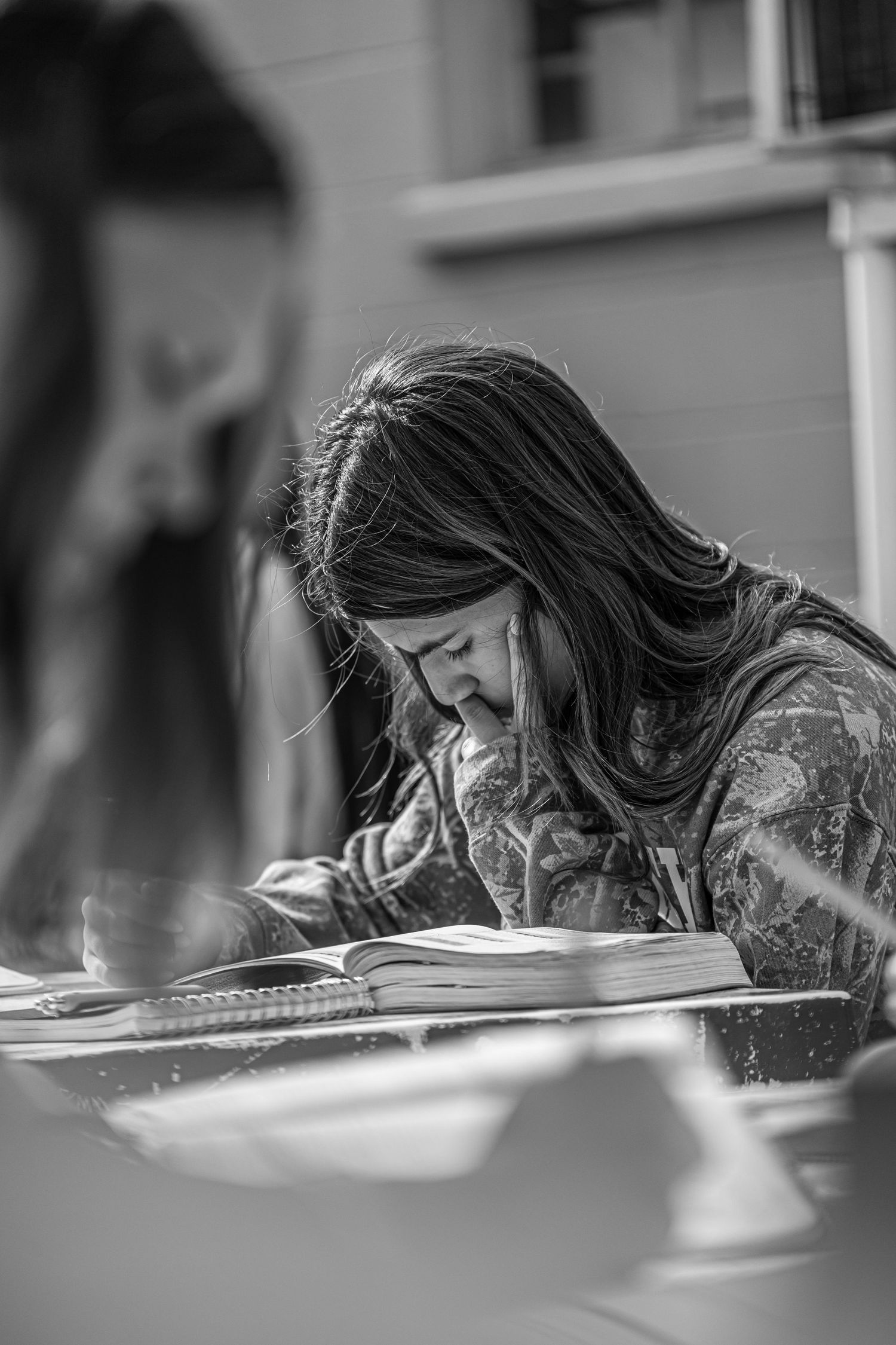 Black and white photo of long-haired student studying and reading book at outdoor table.