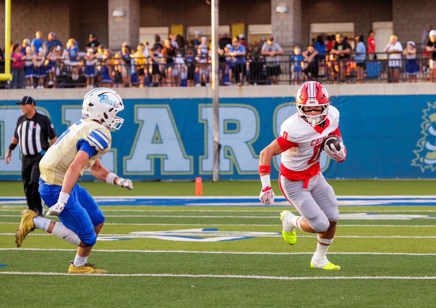 Football player in red uniform runs with the ball past defenders during a college football game.