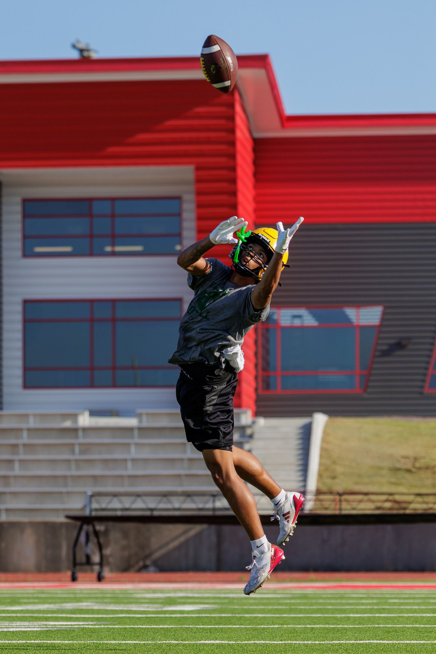 Football player in black uniform jumps to catch a pass during outdoor field practice.