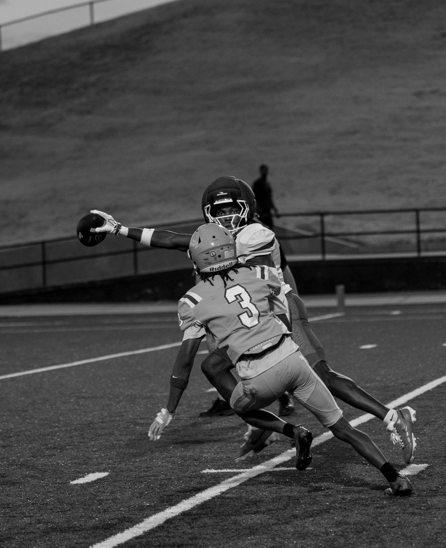 Black and white photo of football players, number 3 defending against a receiver catching a pass during a game.