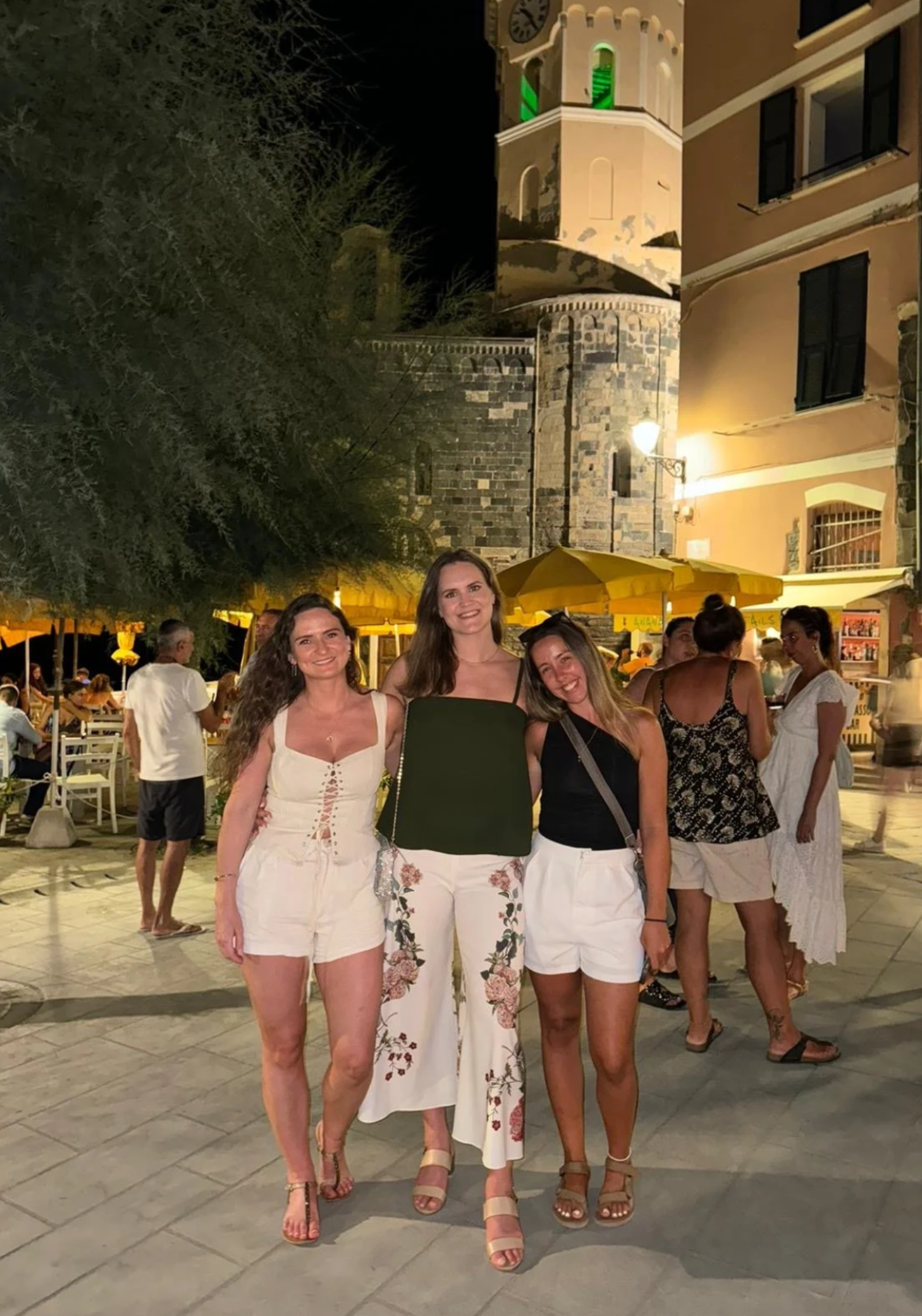 People walking along a Mediterranean town's stone streets at night.