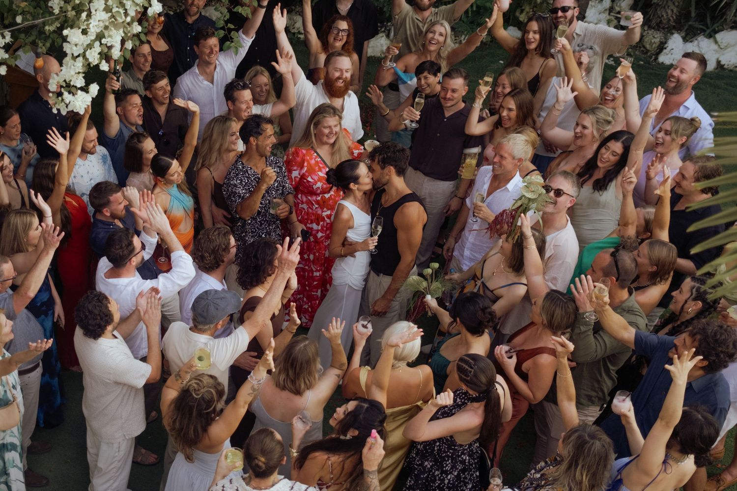 Large crowd of wedding guests celebrating with arms raised in joyful celebration.