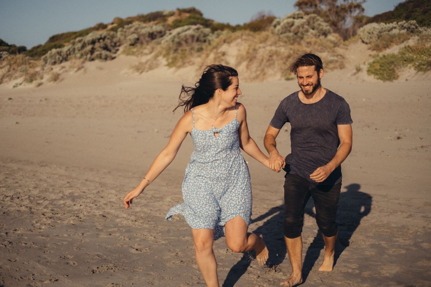 Couple running along a sandy beach hand in hand laughing.