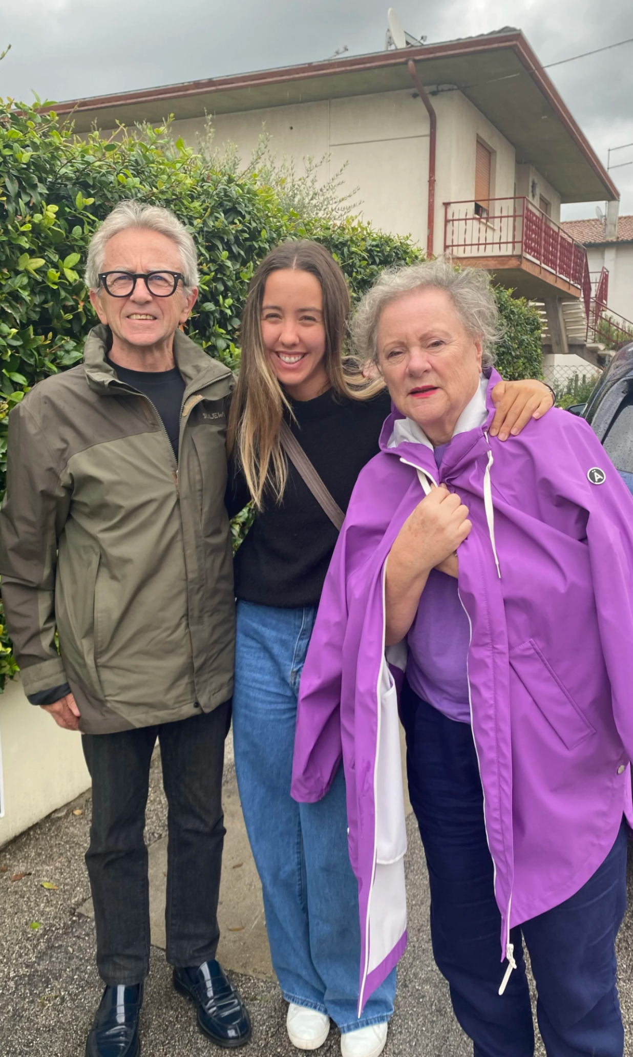 Three people standing together outside a building on a cloudy day.