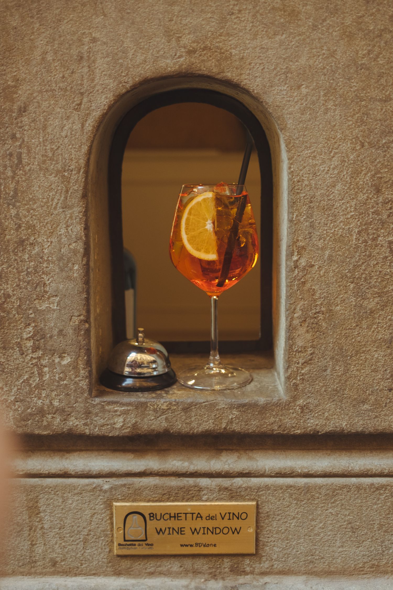 Orange aperitif cocktail displayed in a rustic stone window opening labeled as wine window.