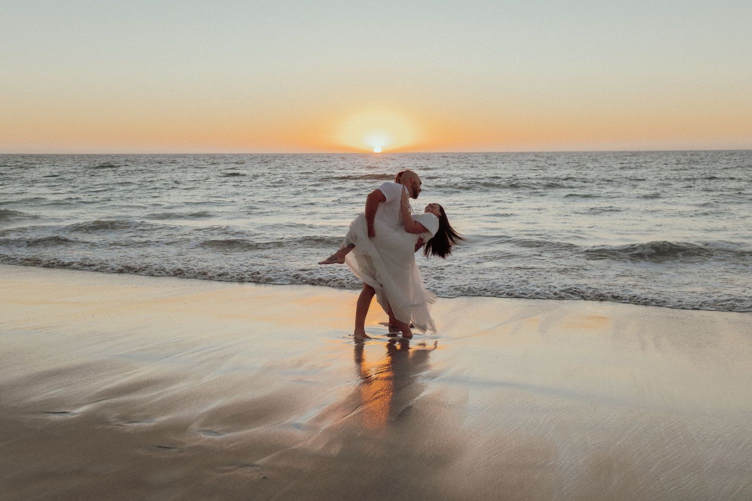 Silhouettes dancing and playing in ocean waves during sunset.