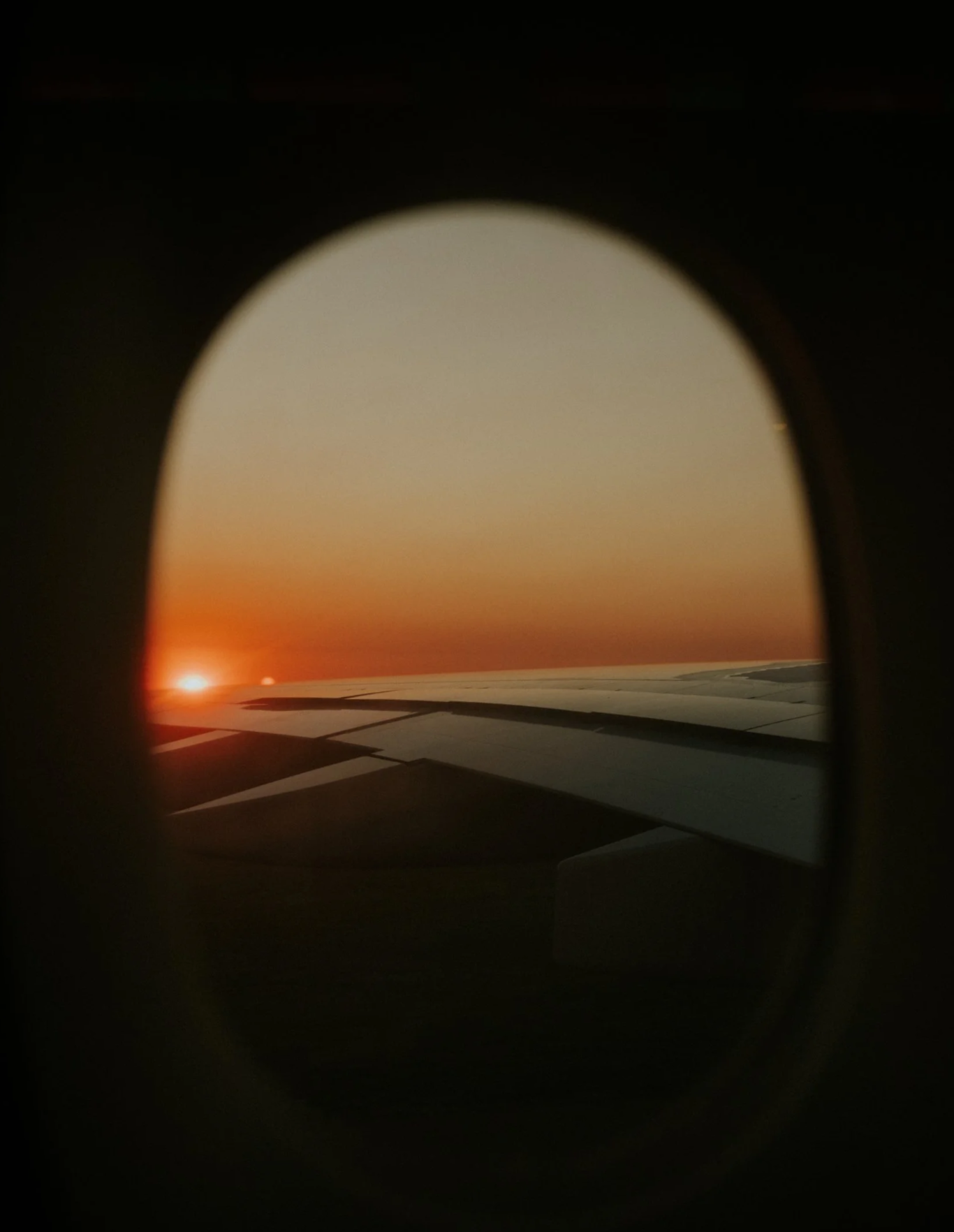 View of an airplane wing and sunset through an aircraft window.