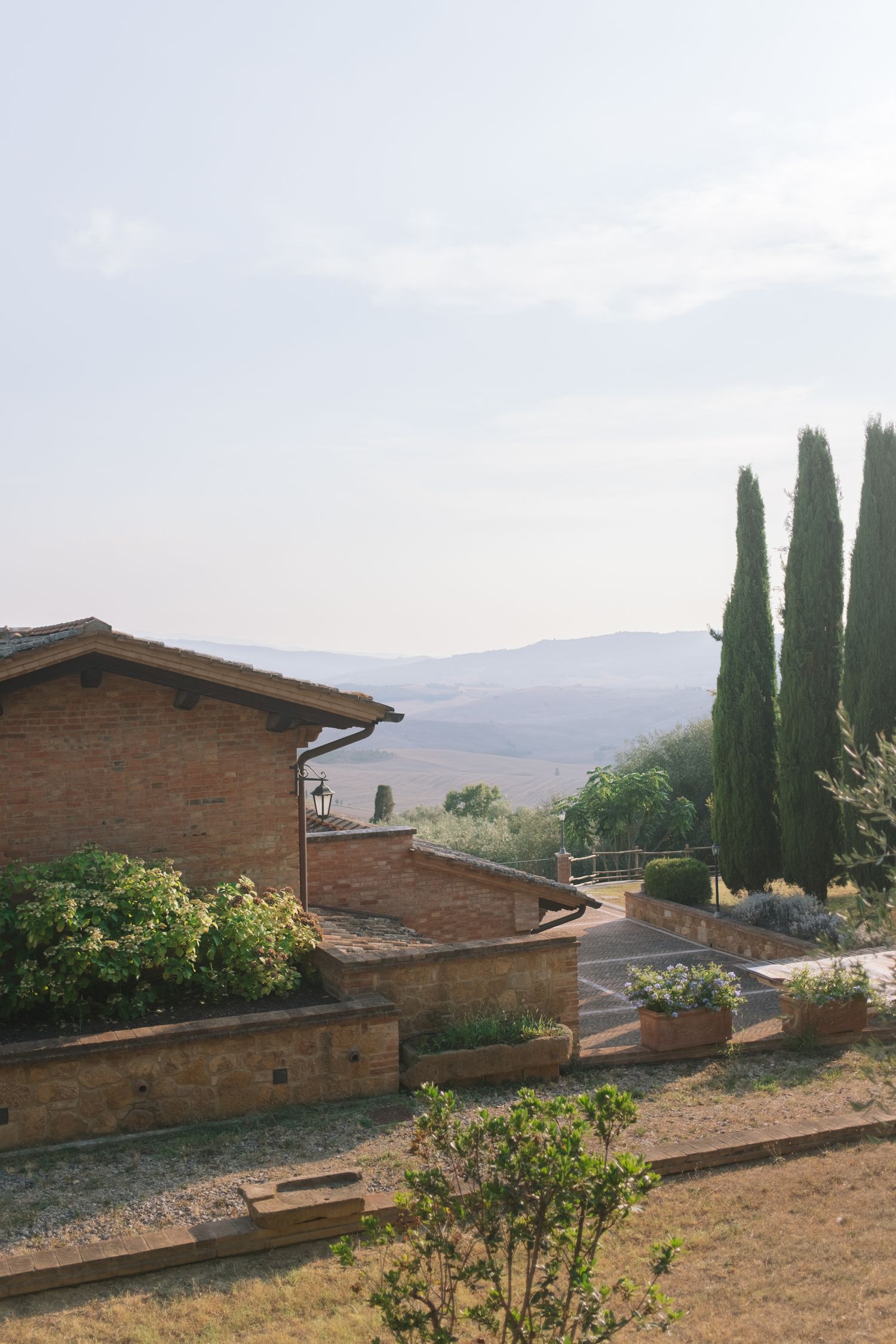 Tuscan landscape with stone buildings and cypress trees against rolling hills.