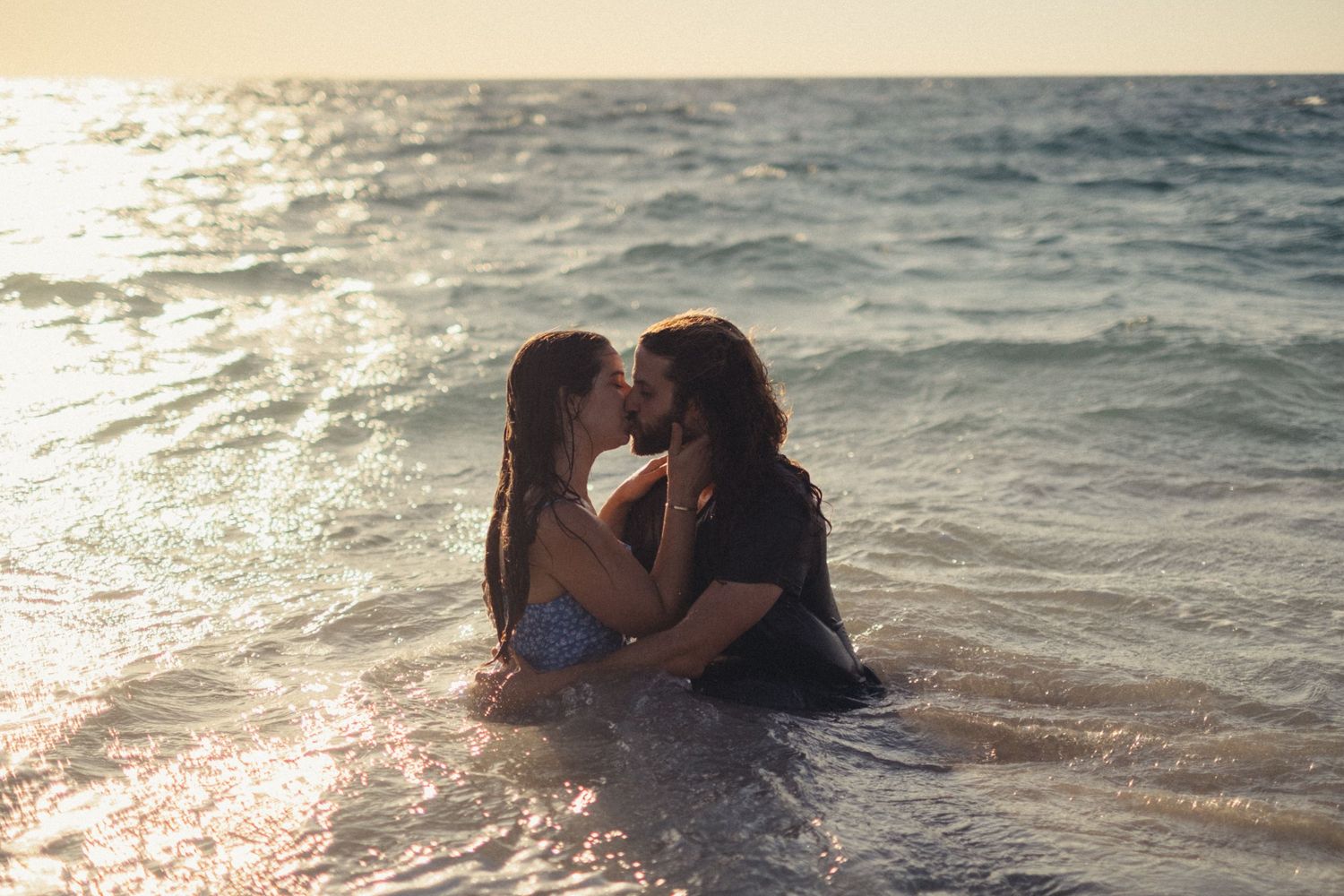 Romantic couple playing in the ocean waves during golden hour.