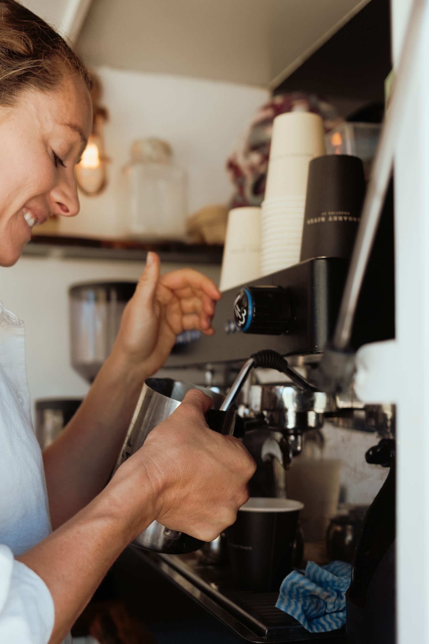 Barista operating an espresso machine in a bright coffee shop setting.