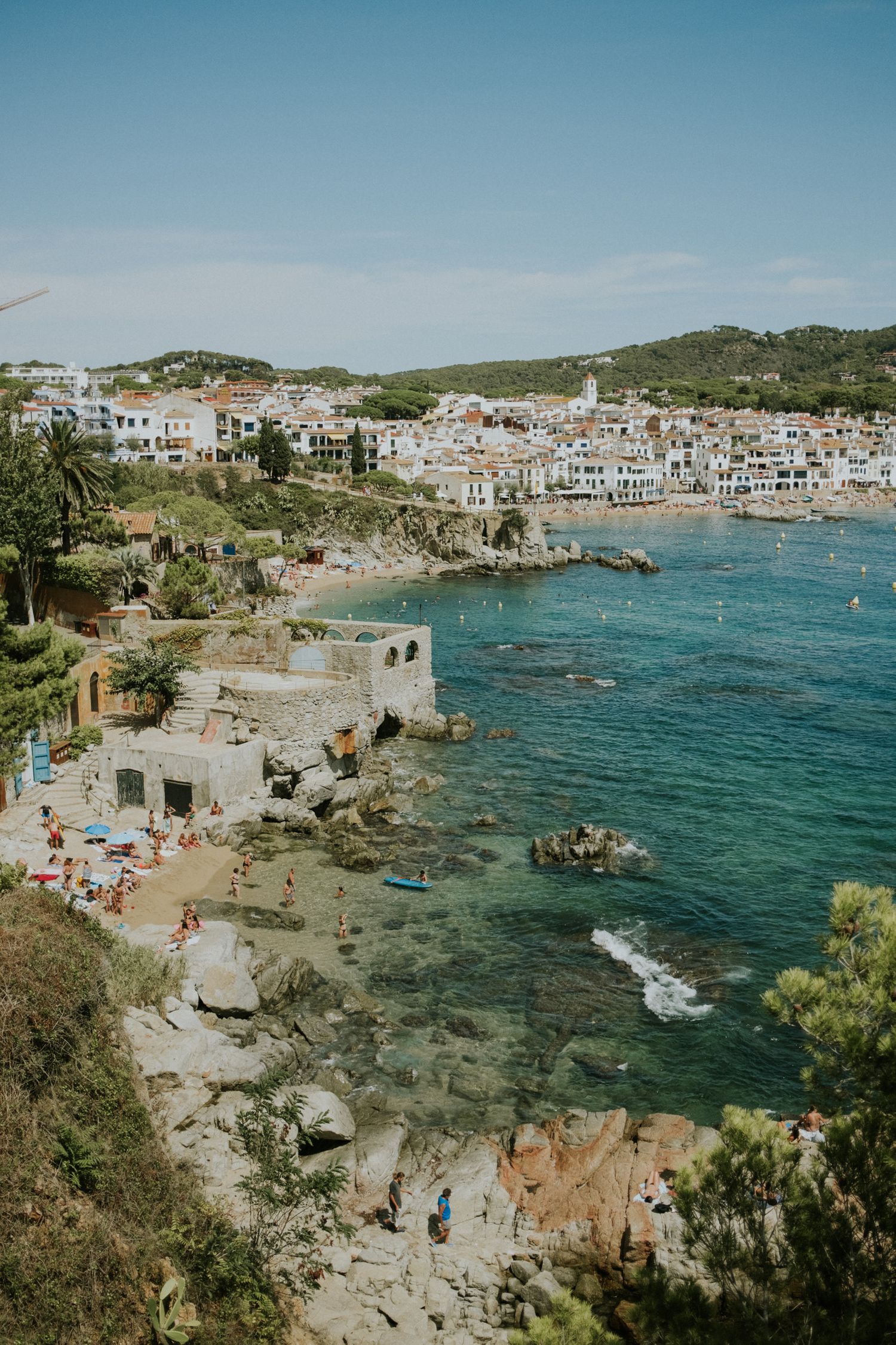 Rocky coastal cove with turquoise waters and beachgoers enjoying a sunny day.