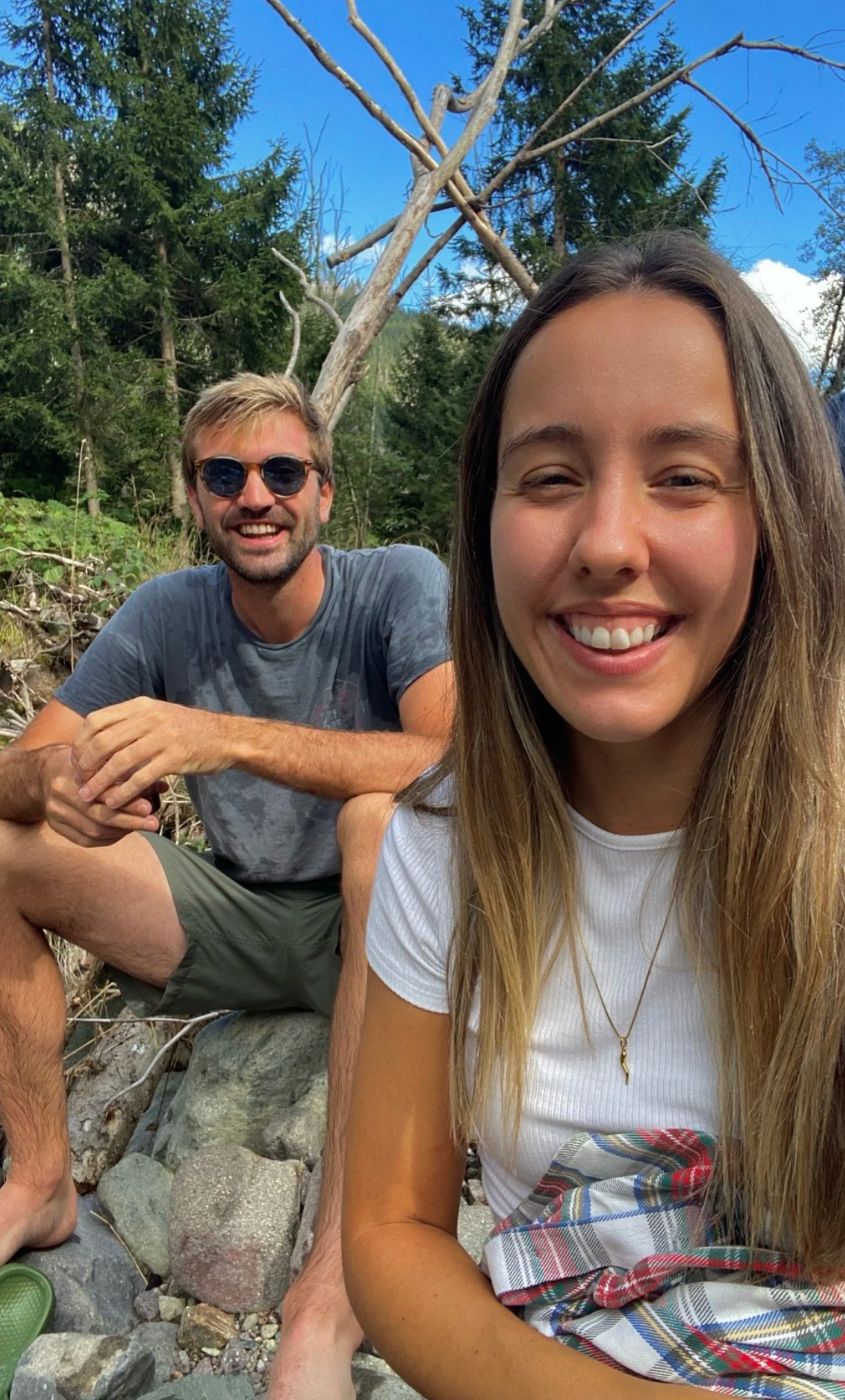 Friends relaxing on rocky terrain surrounded by trees on a sunny day.