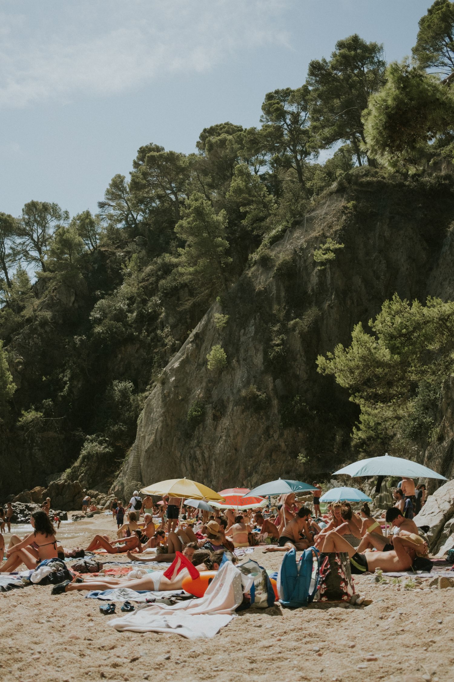 Crowded beach with sunbathers and colorful umbrellas under steep cliffs.