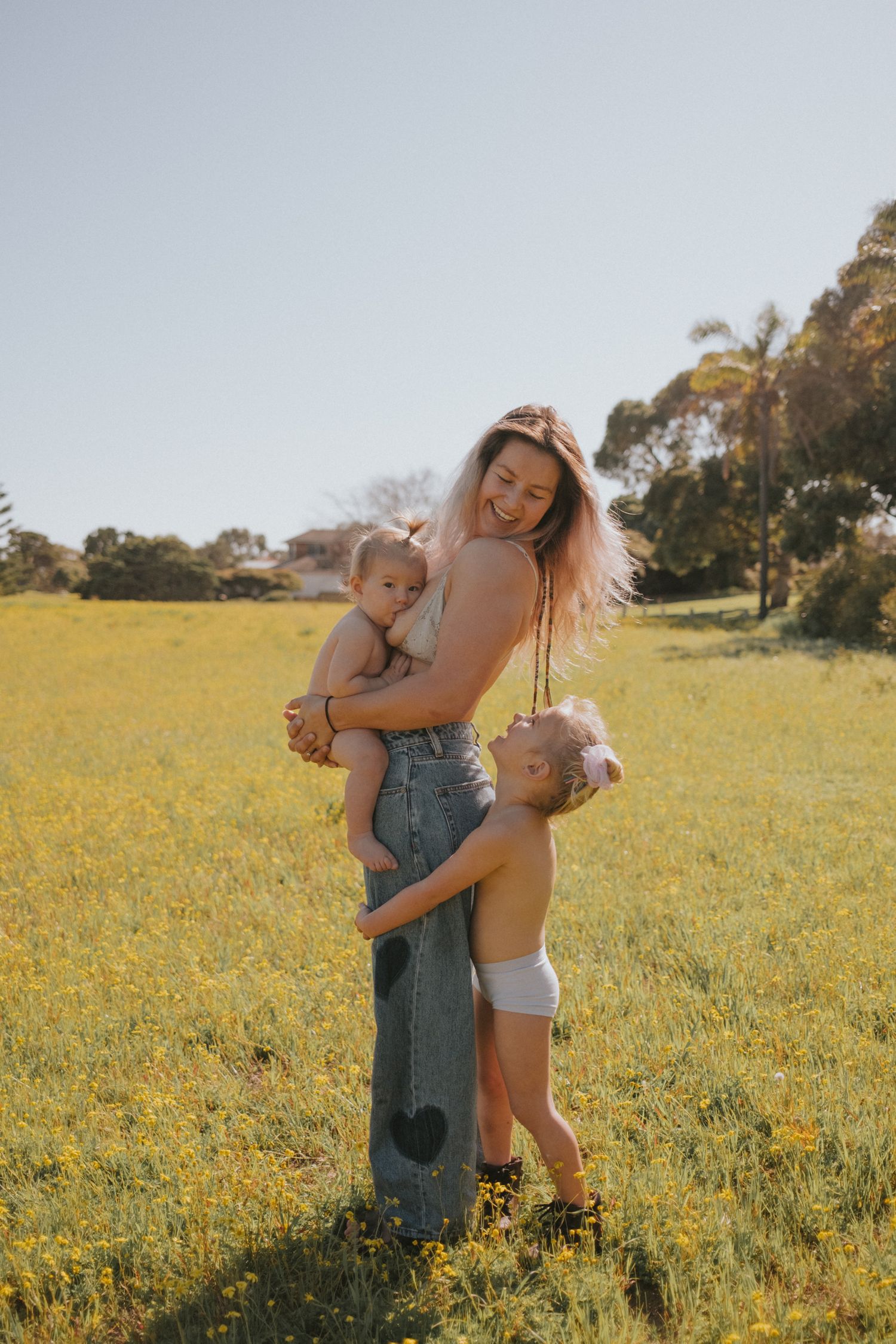 Mum with her daughters embracing in a sunny yellow wildflower field on a bright afternoon.