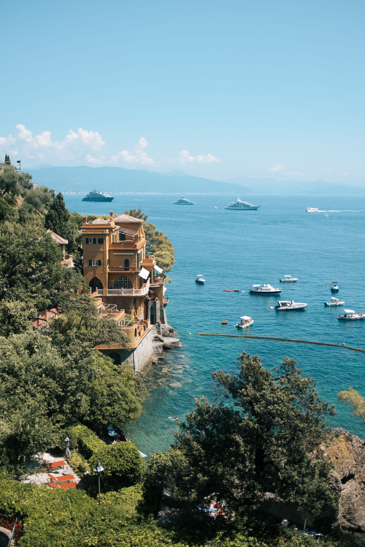Luxury villas and boats dot the Mediterranean coastline of Portofino, Italy with azure waters and clear blue skies.