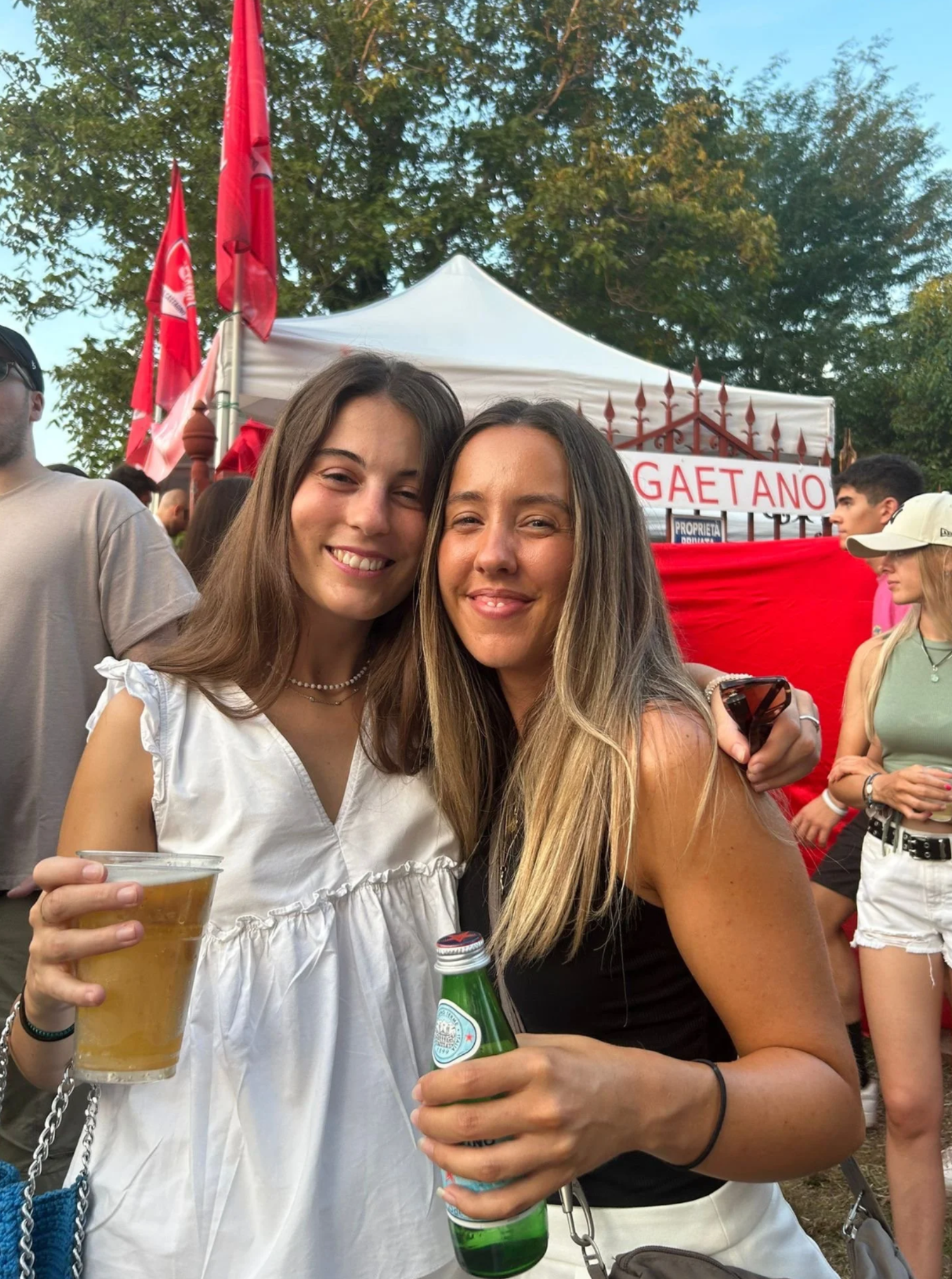 Friends enjoying drinks at an outdoor festival with red banners visible.