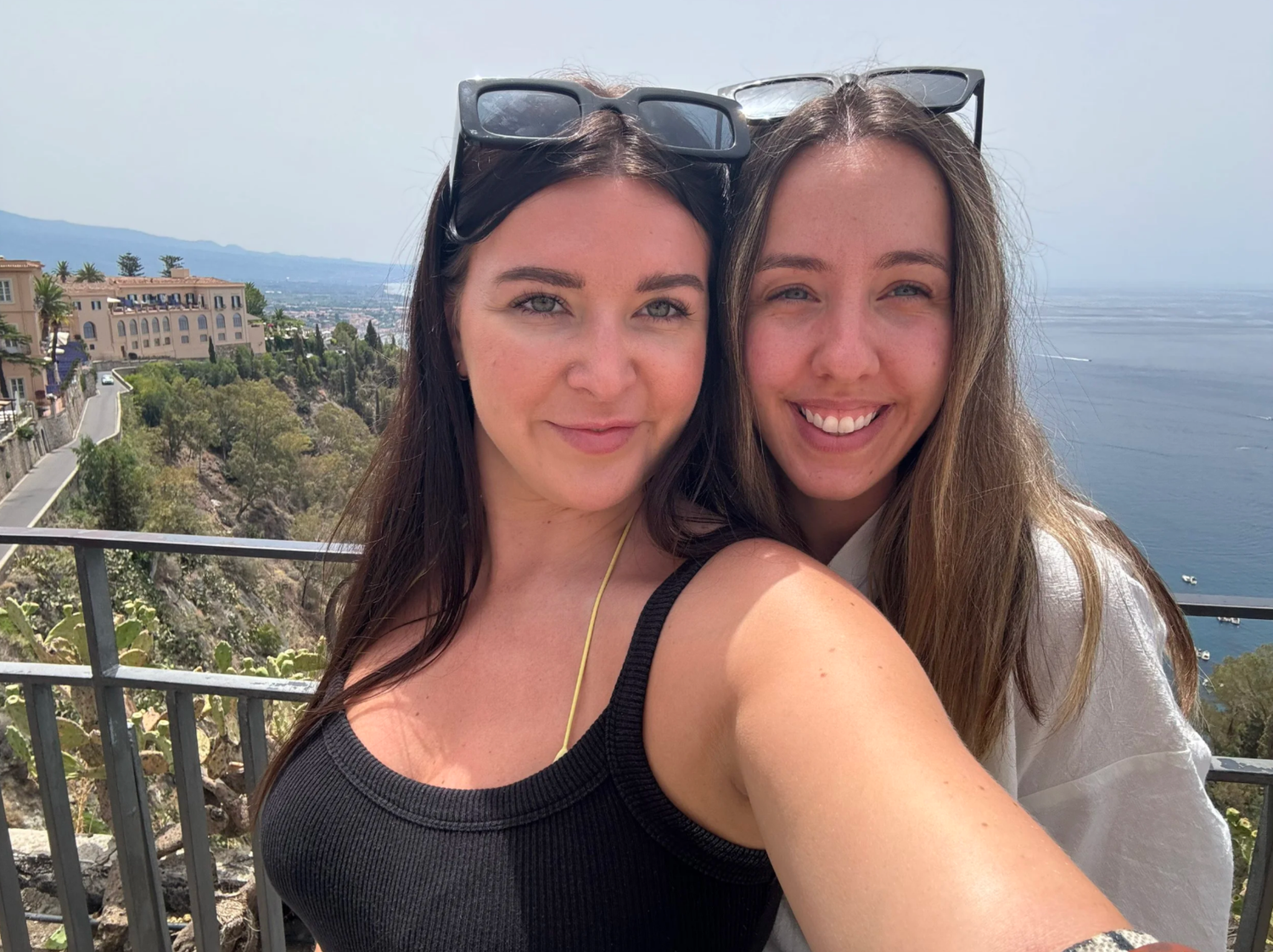 Friends taking selfies with a scenic coastal view and mountains in the background.