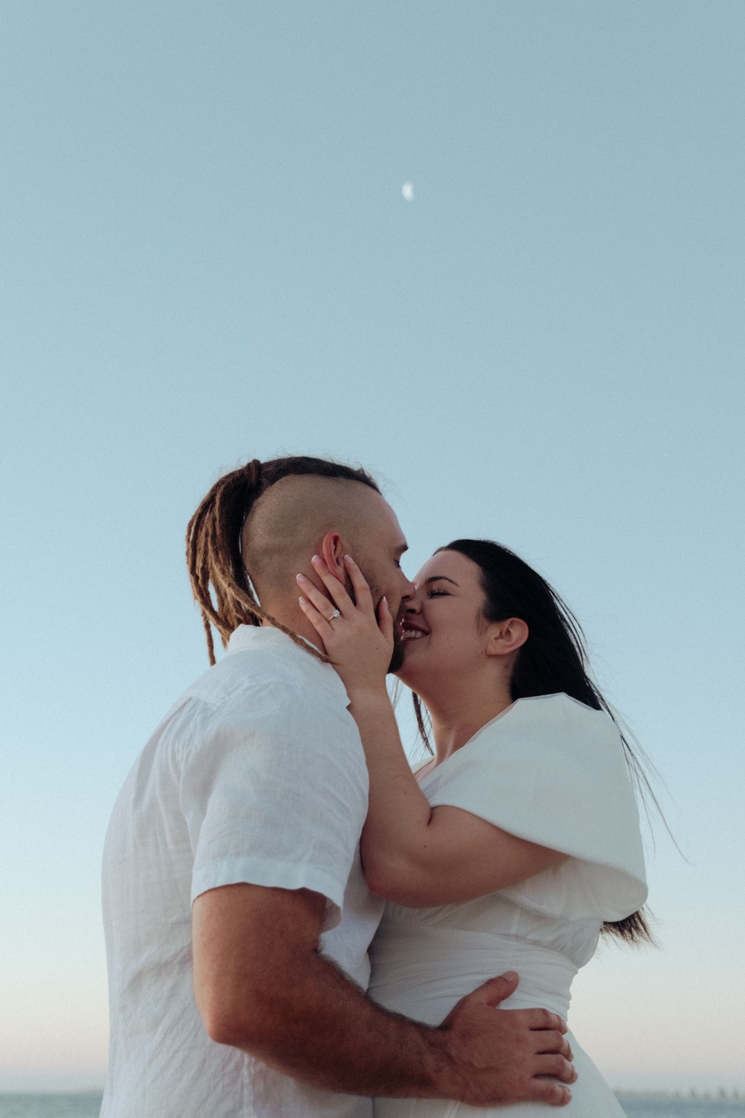 A romantic couple sharing an intimate moment against a bright blue sky background.