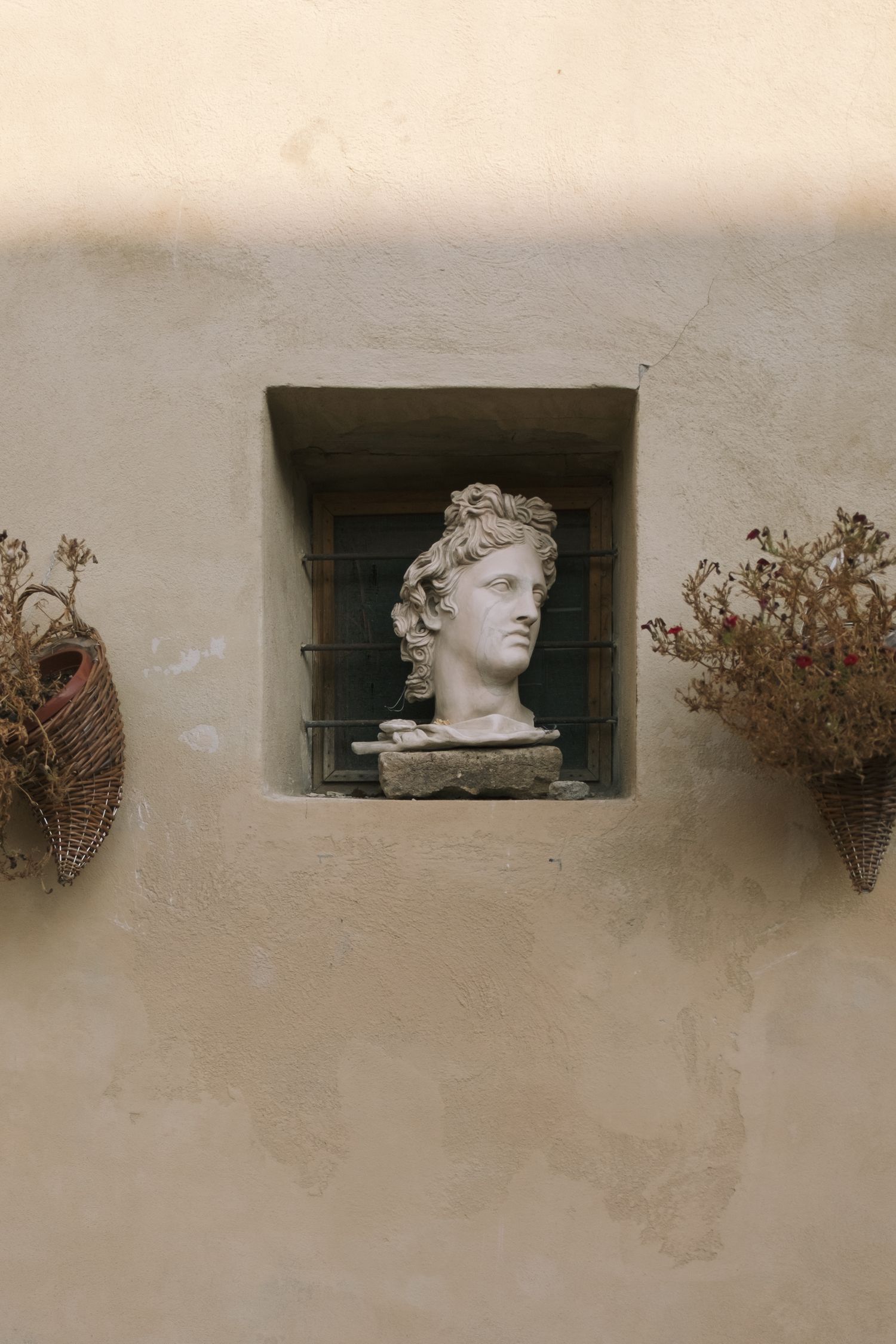 Classical stone busts and dried flowers displayed in wall niches of an Italian building.